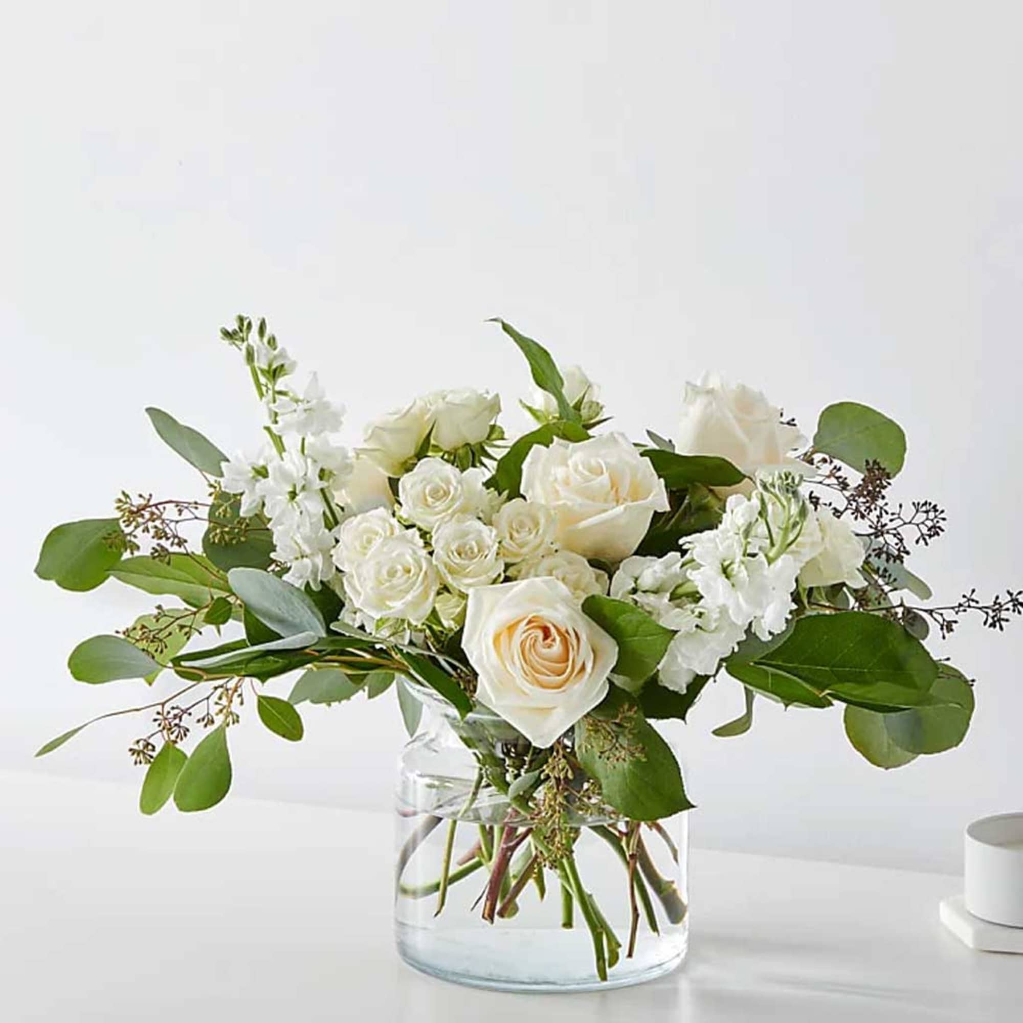 White roses and white blooms in a clear glass vase with greenery