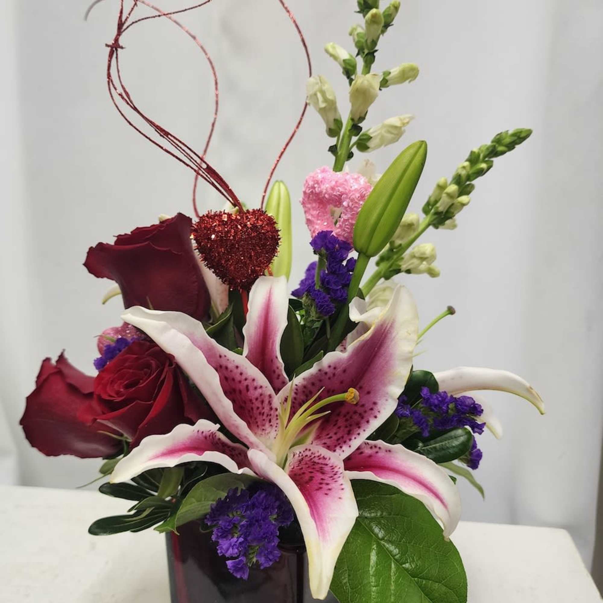 Mixed bouquet with lilies, roses, and purple filler in a dark glass vase