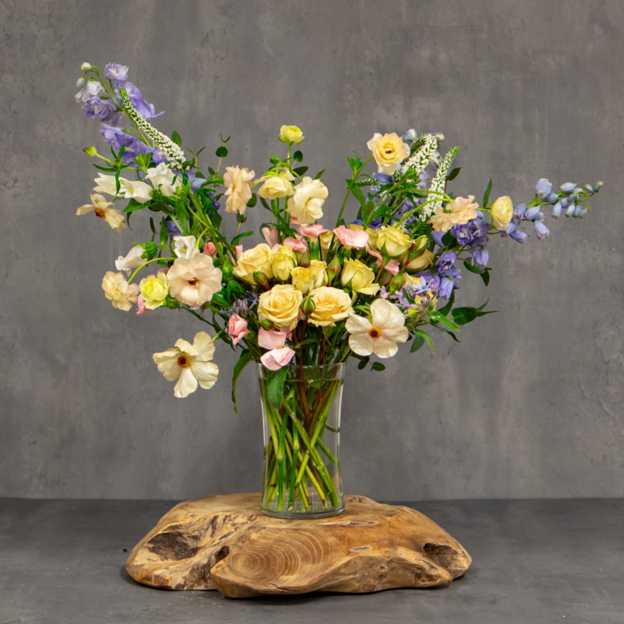 Mixed pastel flowers in a clear glass vase on a wooden base