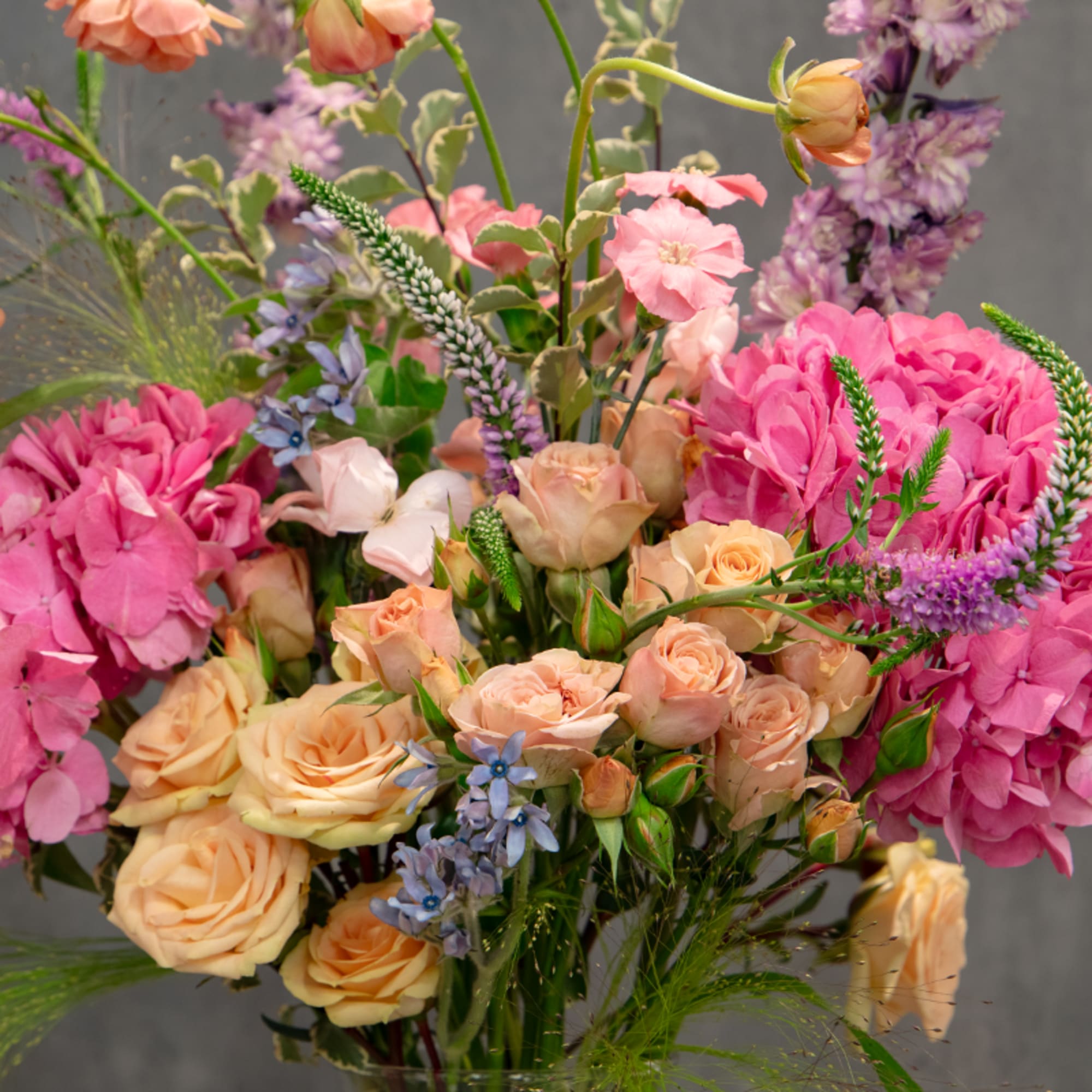 Mixed bouquet of peach roses, pink blooms, and purple flowers in a glass vase