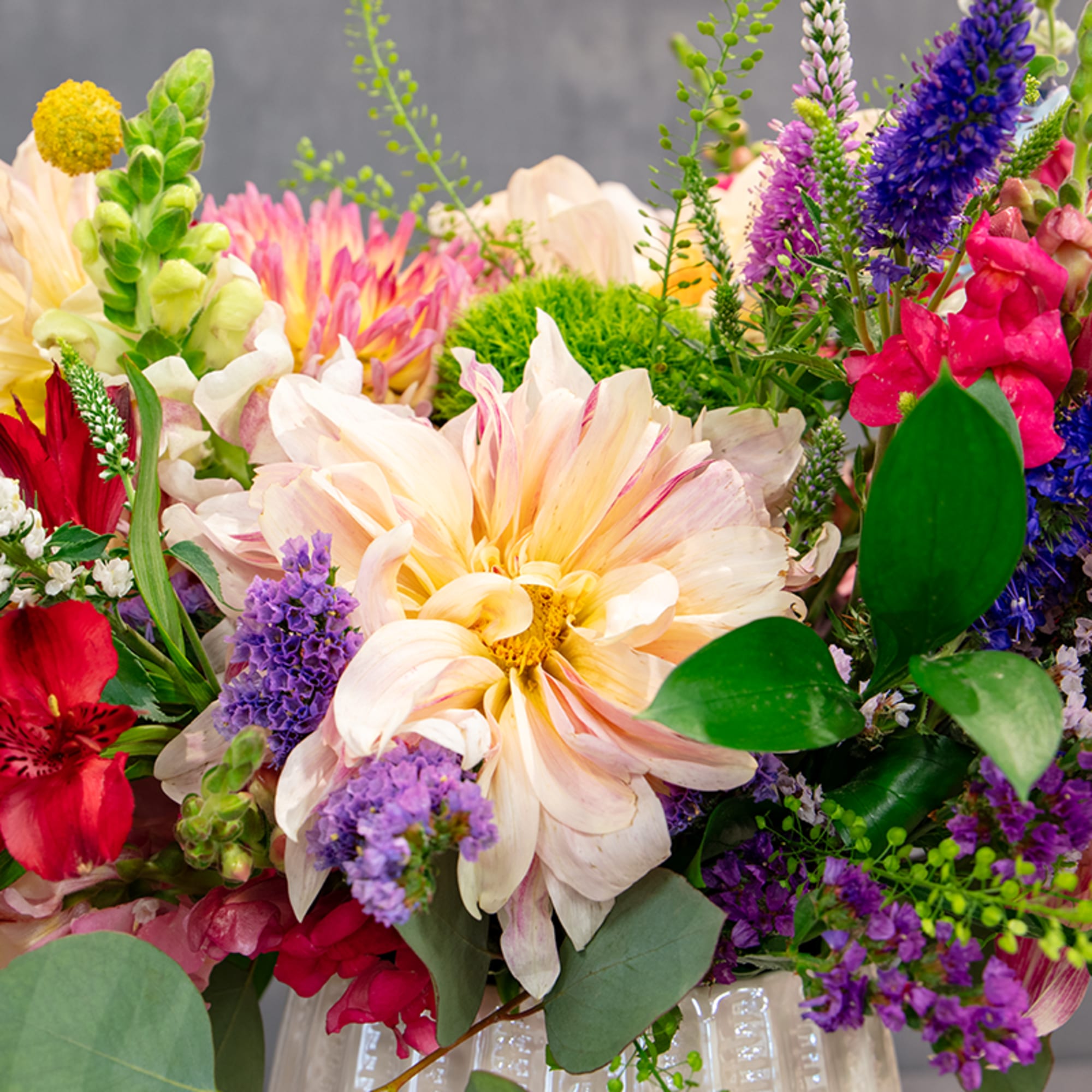 Mixed bouquet with peach dahlias, purple spikes, and red blooms in a white vase
