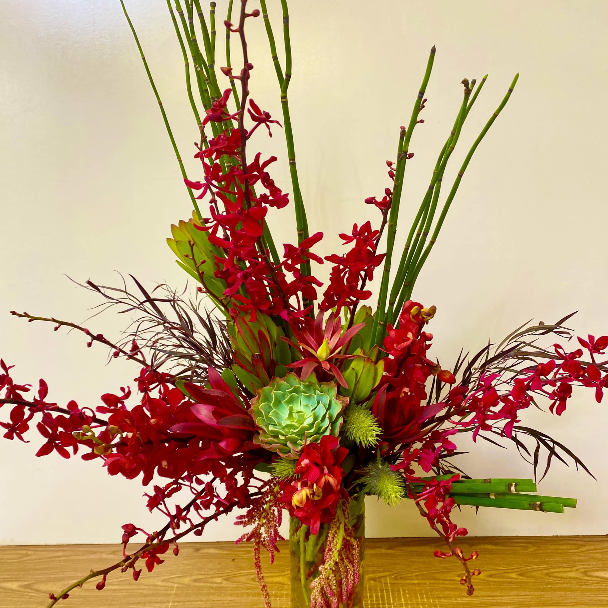 Tall red floral arrangement in a glass vase with green accents