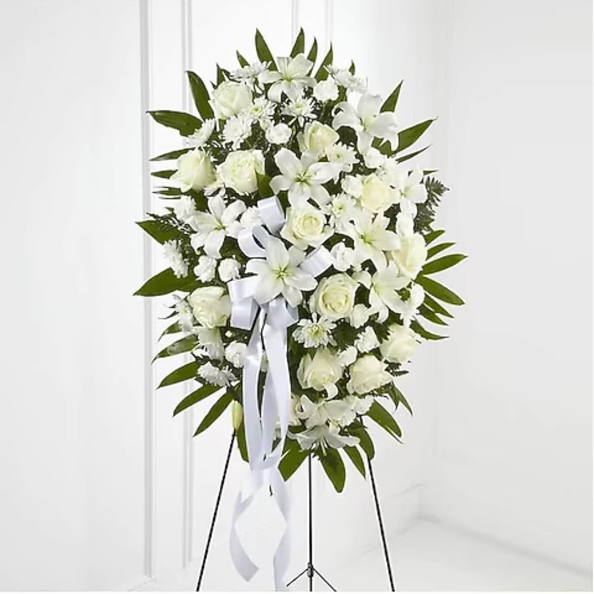 White funeral spray with lilies, roses, and a ribbon on a stand