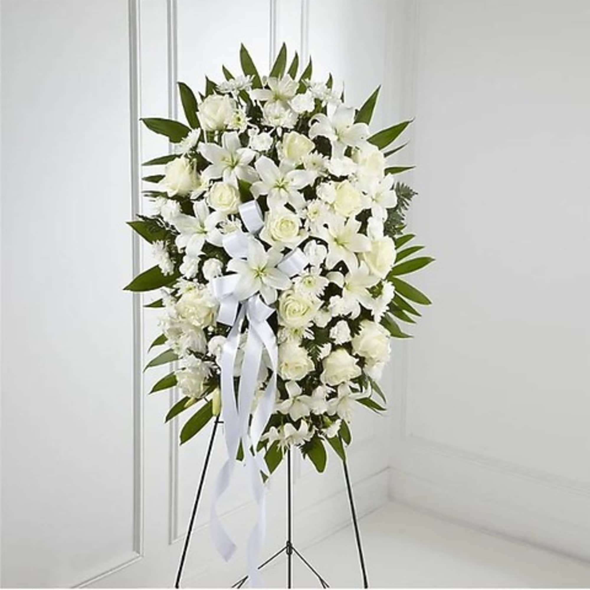 White floral standing wreath on a black easel with a ribbon bow