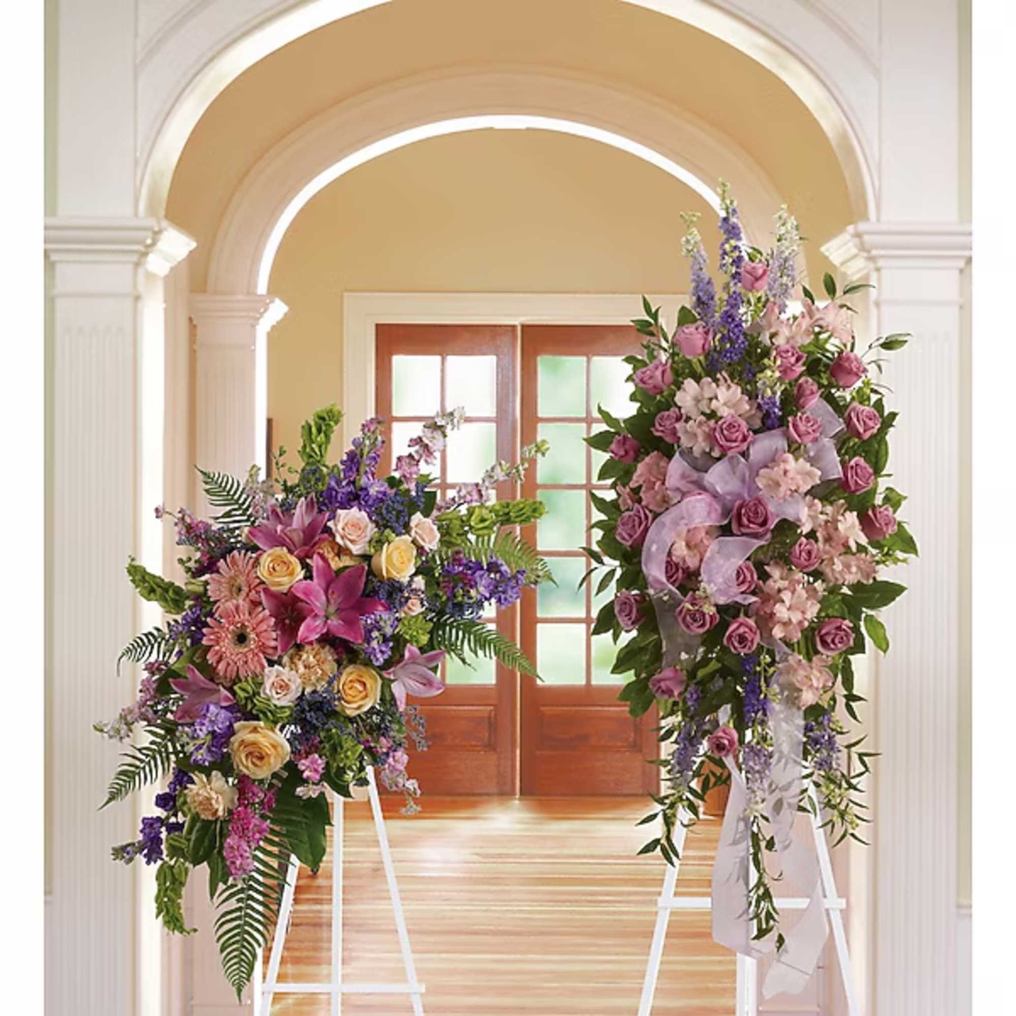 Two large floral standing arrangements with pink, purple, and cream flowers on white easels.