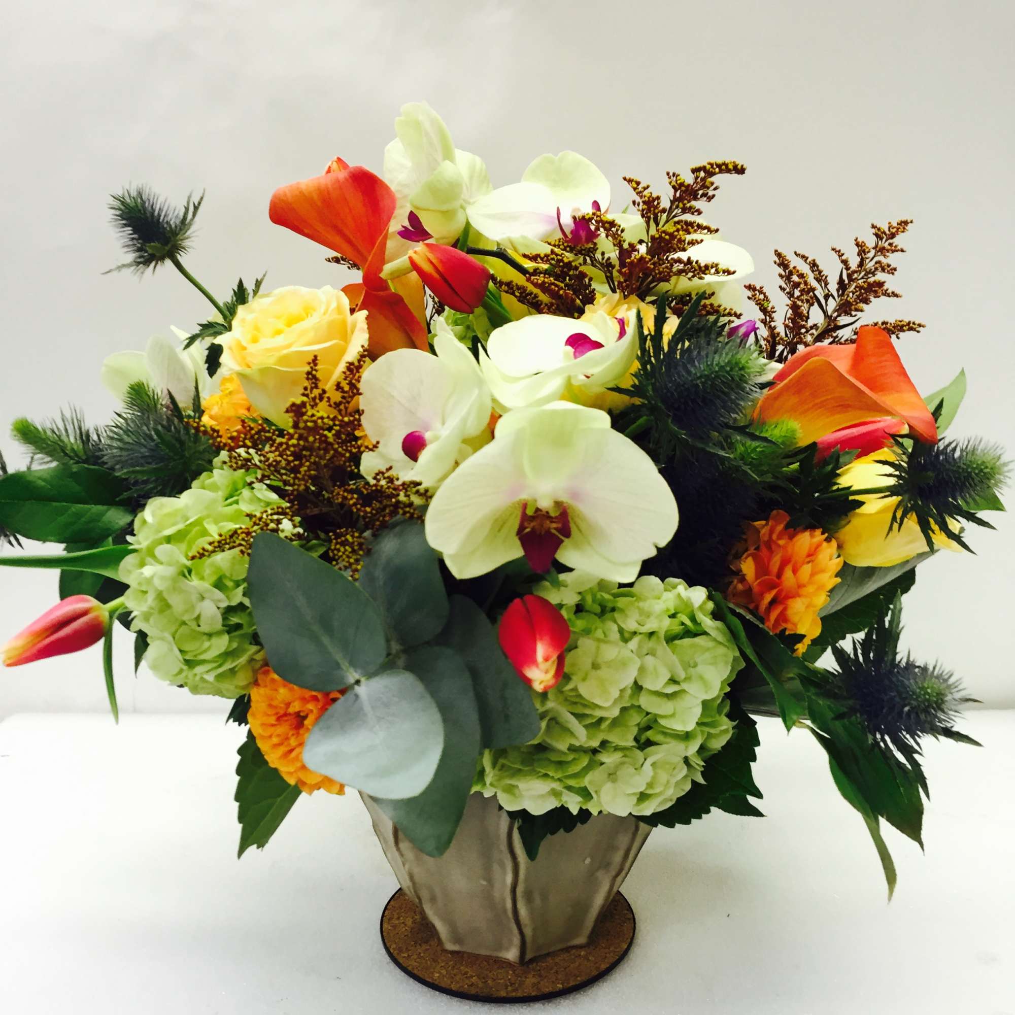 Mixed bouquet with orchids, roses, hydrangeas, and orange calla lilies in a metal vase