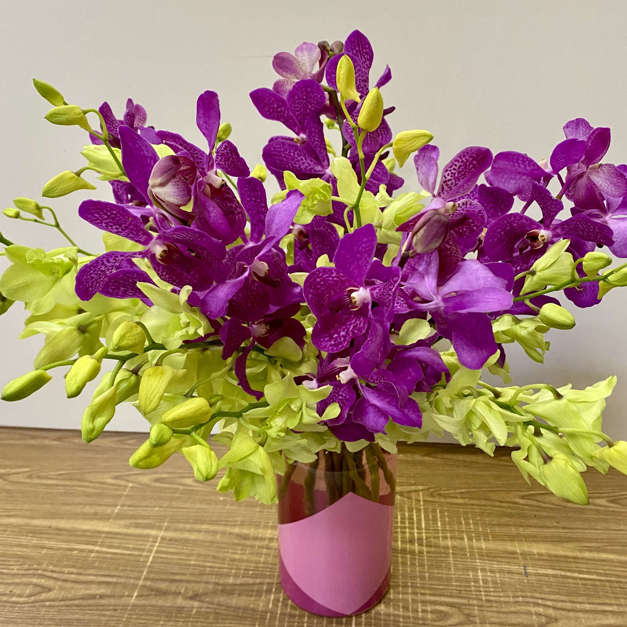 Purple and lime orchid arrangement in a pink vase