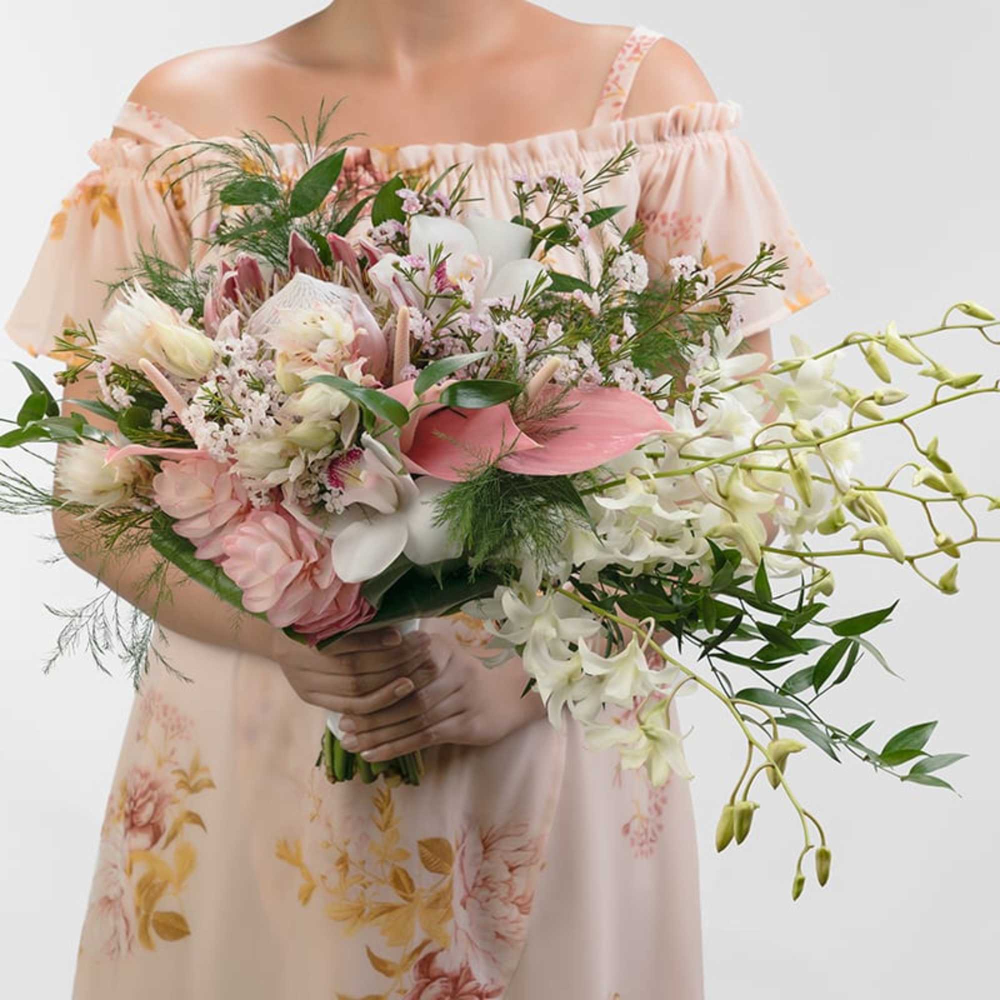 Hand-tied bouquet of pink and white flowers with cascading orchids held by a person in a floral dress