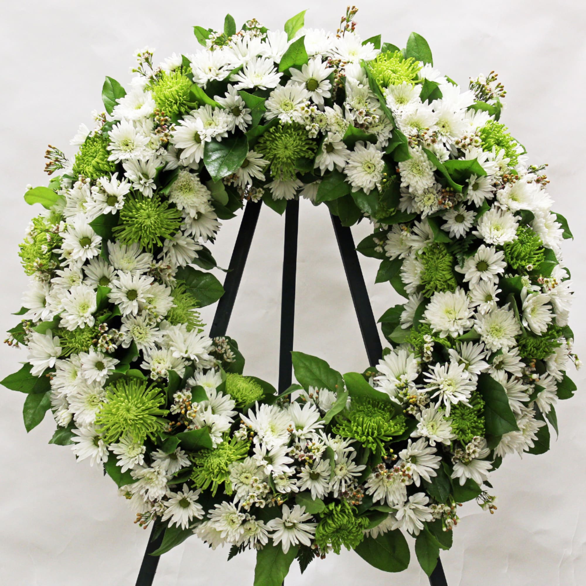 Large white and green floral wreath displayed on a black metal easel
