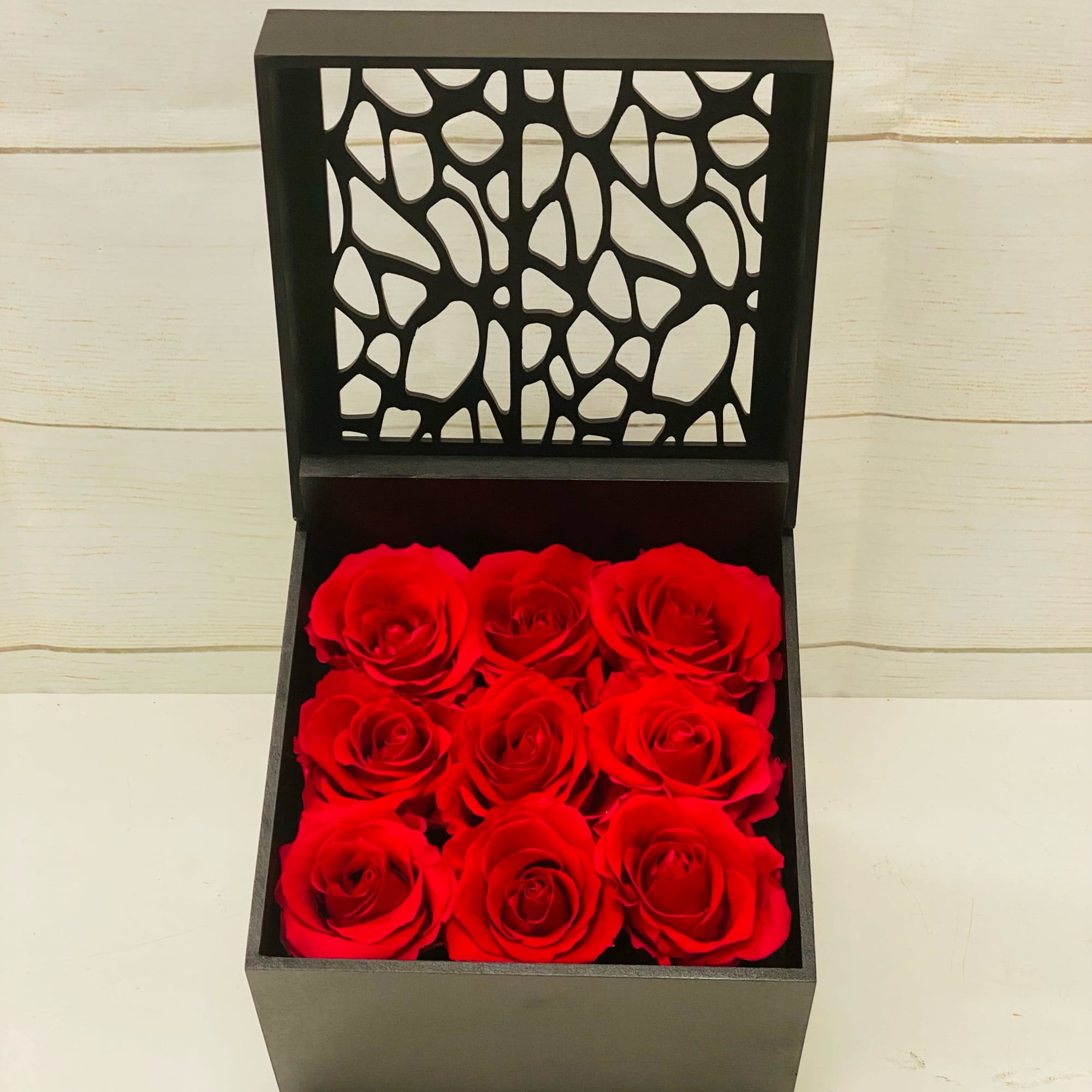 Black box of nine red roses with an upright lid featuring a cutout pattern.
