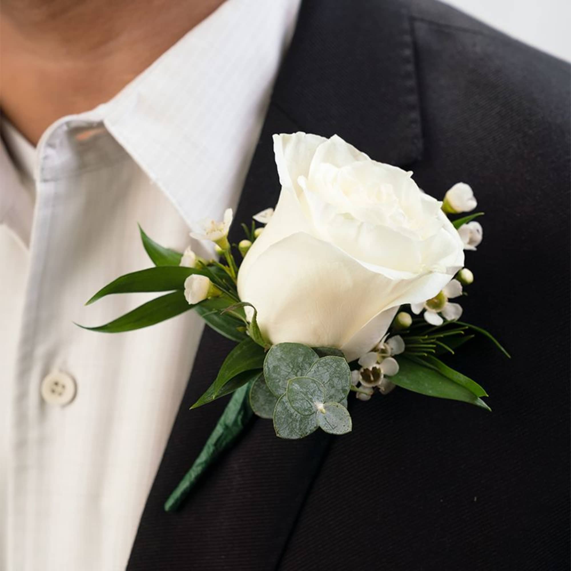 White rose boutonniere with small white accent flowers on a black suit lapel