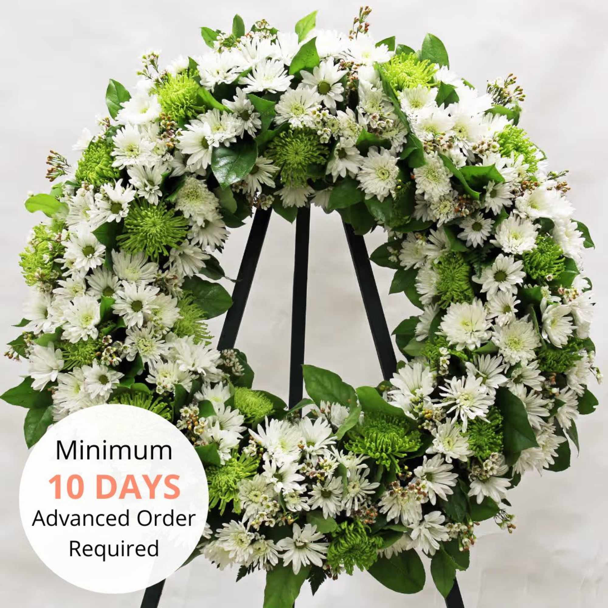 Large white and green chrysanthemum wreath on a black metal easel against a plain background