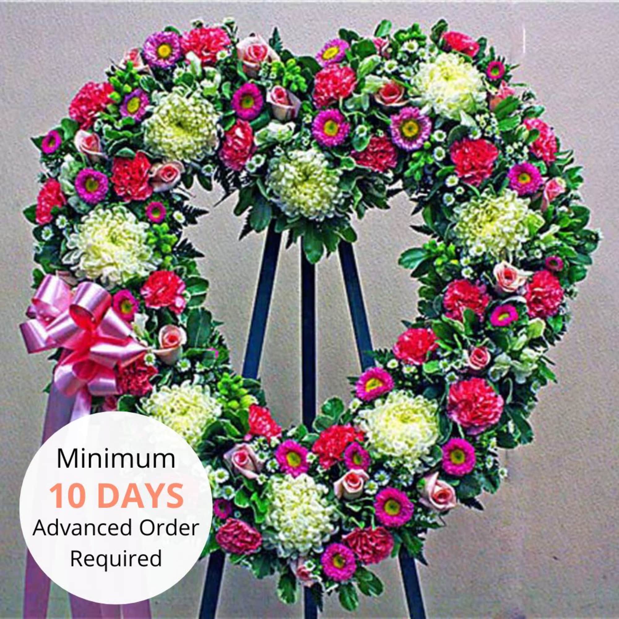 Tall heart-shaped standing wreath of pink and white flowers with a pink bow on an easel
