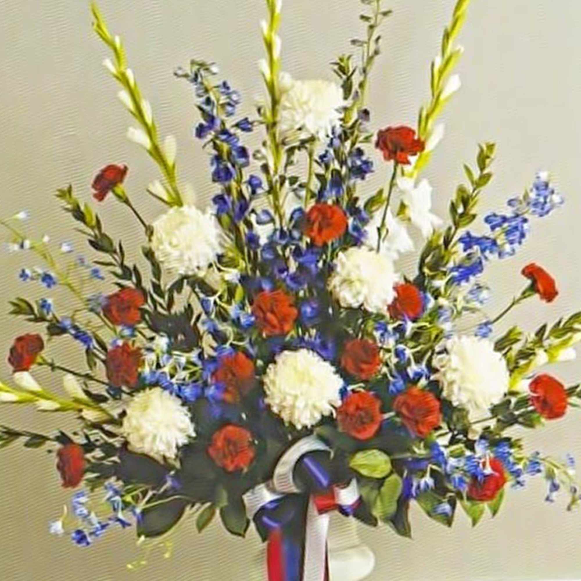 Tall red, white, and blue floral arrangement in a white urn with a patriotic ribbon
