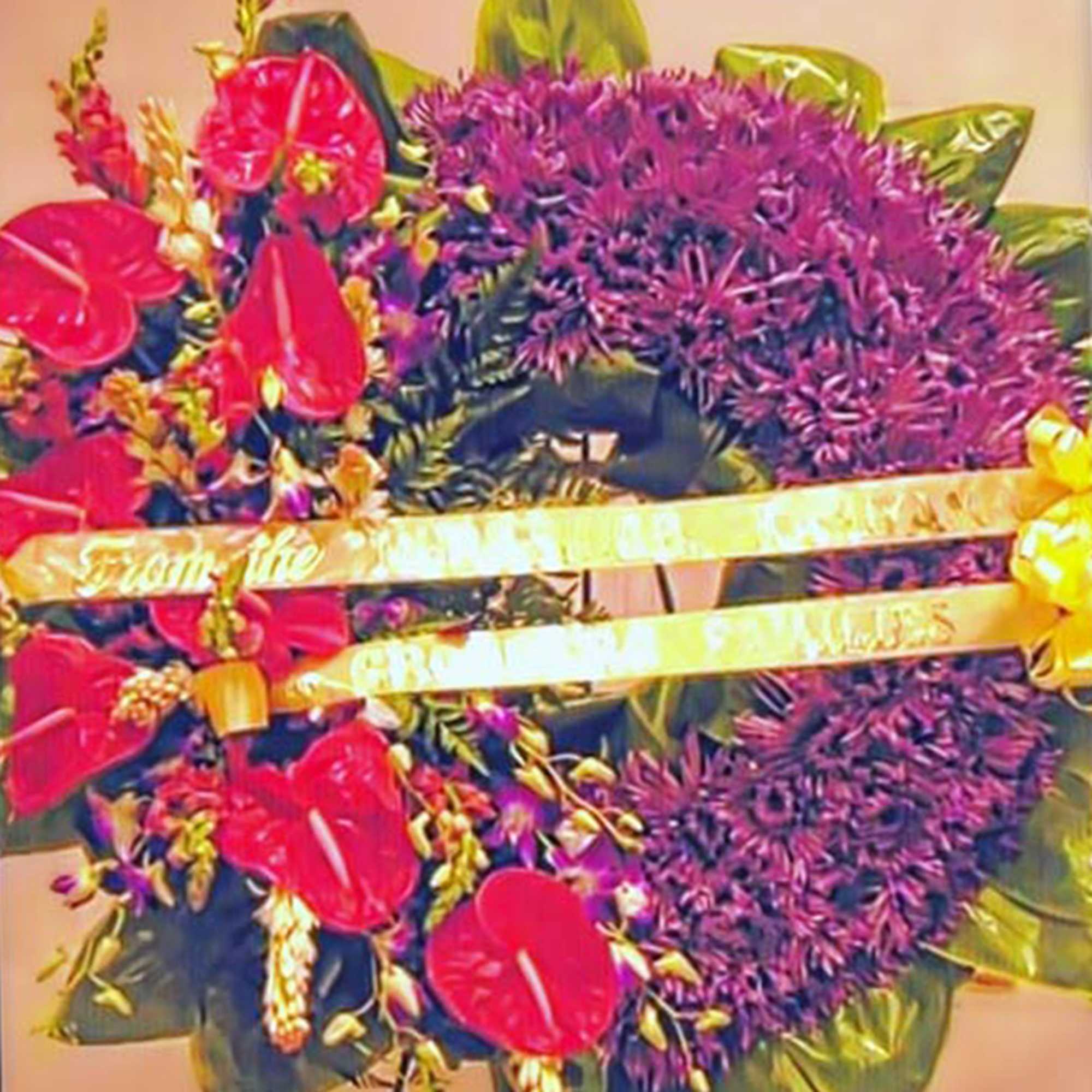 Standing wreath with purple flowers, red tropical blooms, and a yellow ribbon banner.