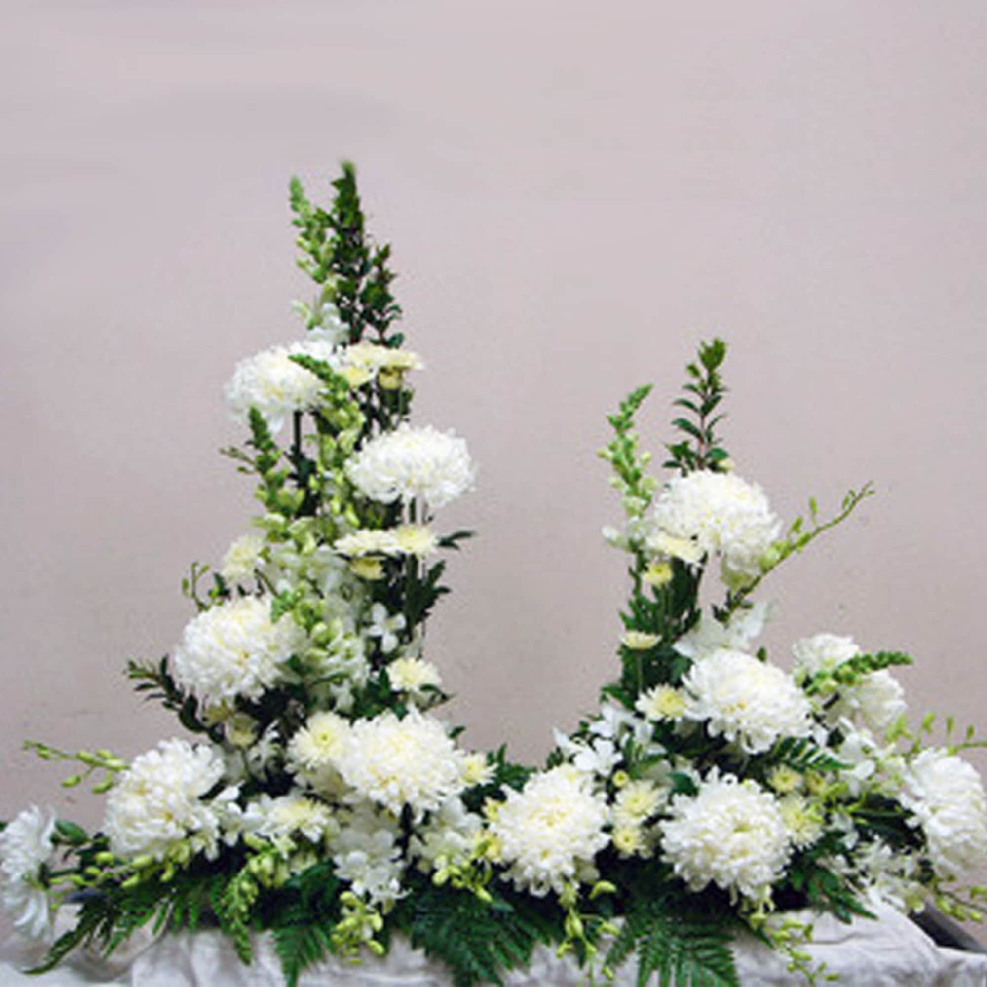 Pair of white floral arrangements with tall spires and round blooms in a symmetrical design