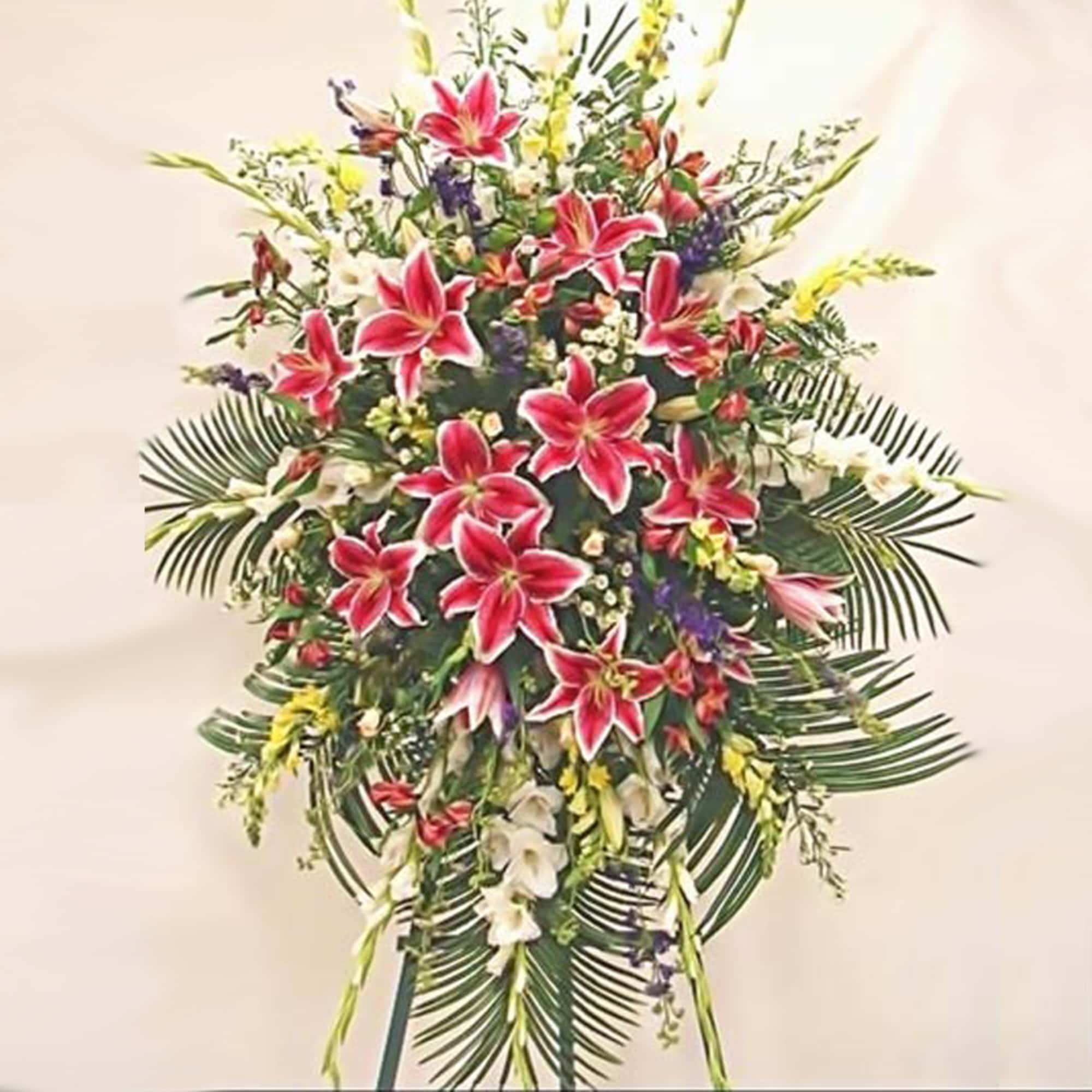 Tall standing spray with pink lilies and mixed flowers on a leafy easel.