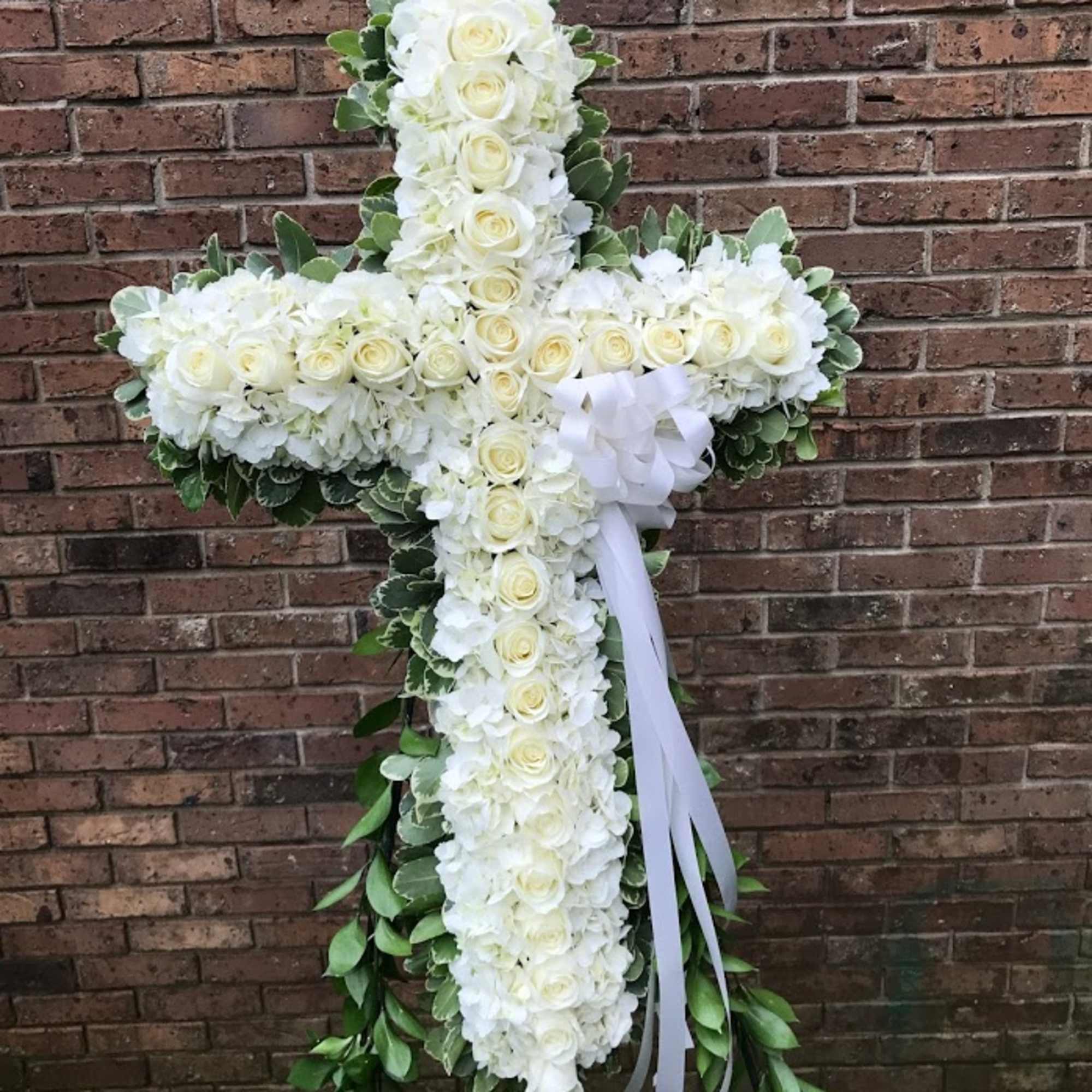 Standing cross-shaped arrangement of white roses and hydrangeas with ribbon on an easel