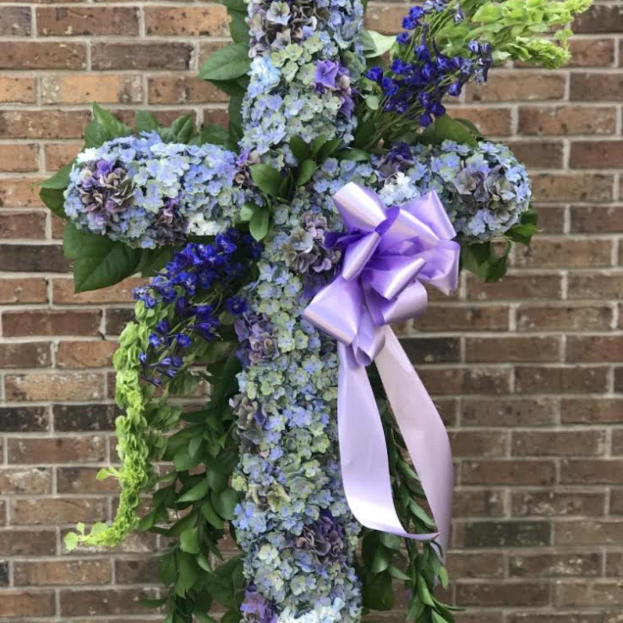 Tall floral cross of blue and purple flowers with a lavender bow.