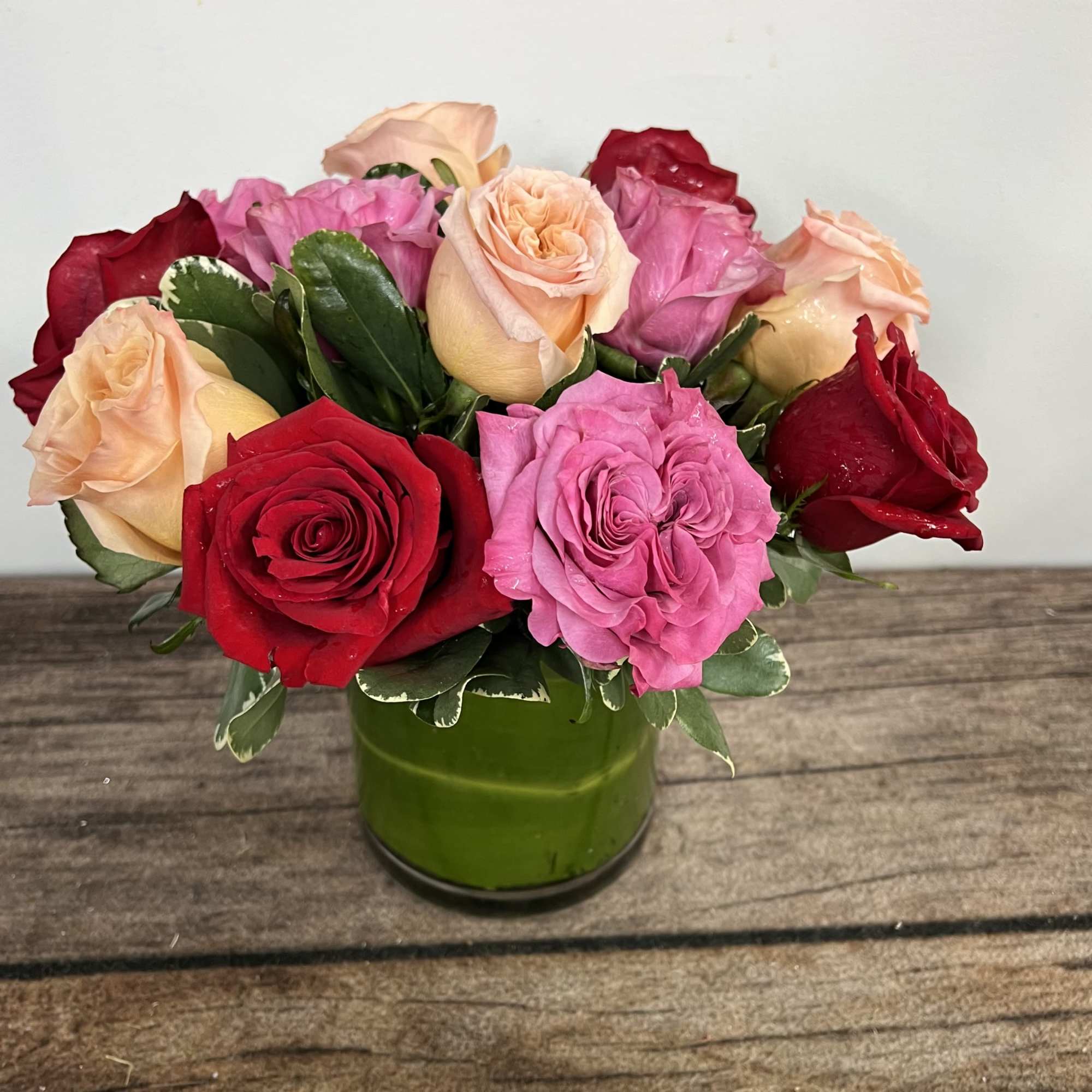 Short arrangement of red, pink, and peach roses in a green glass cylinder vase