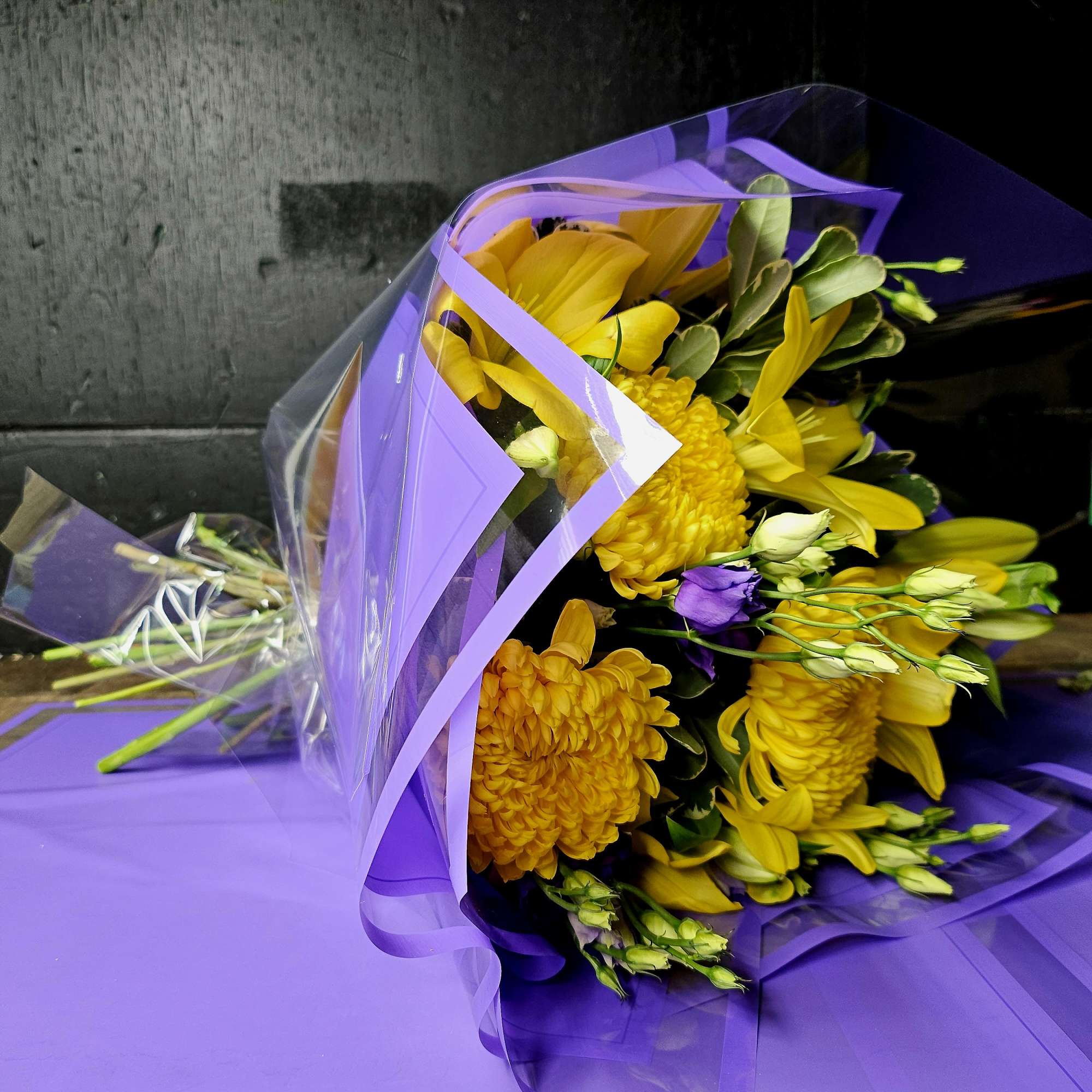 Yellow bouquet wrapped in purple paper with clear plastic