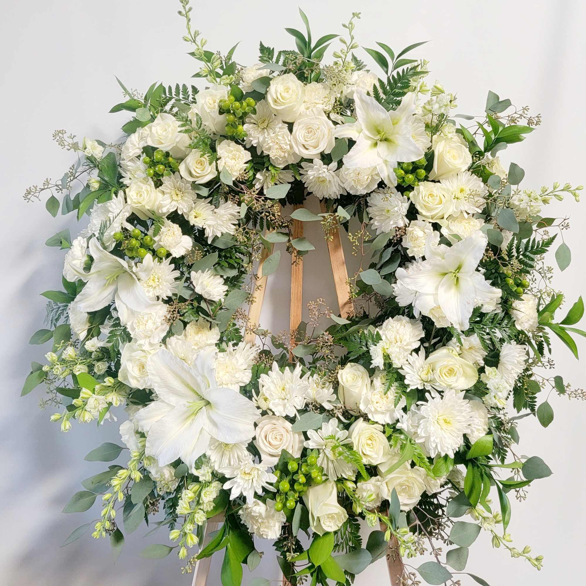 White floral wreath on a wooden easel with lilies and roses