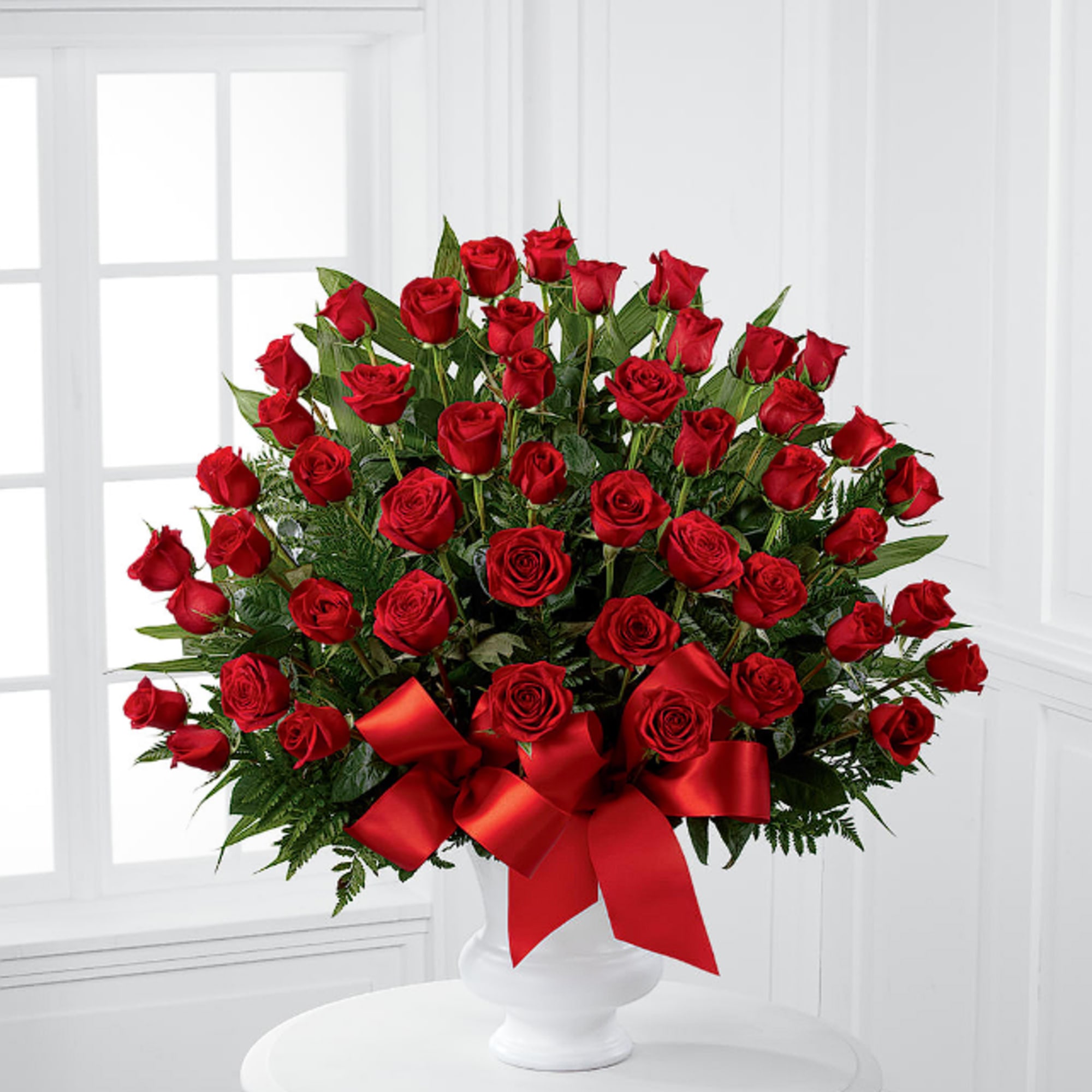 Red roses arranged in a white vase with a red ribbon