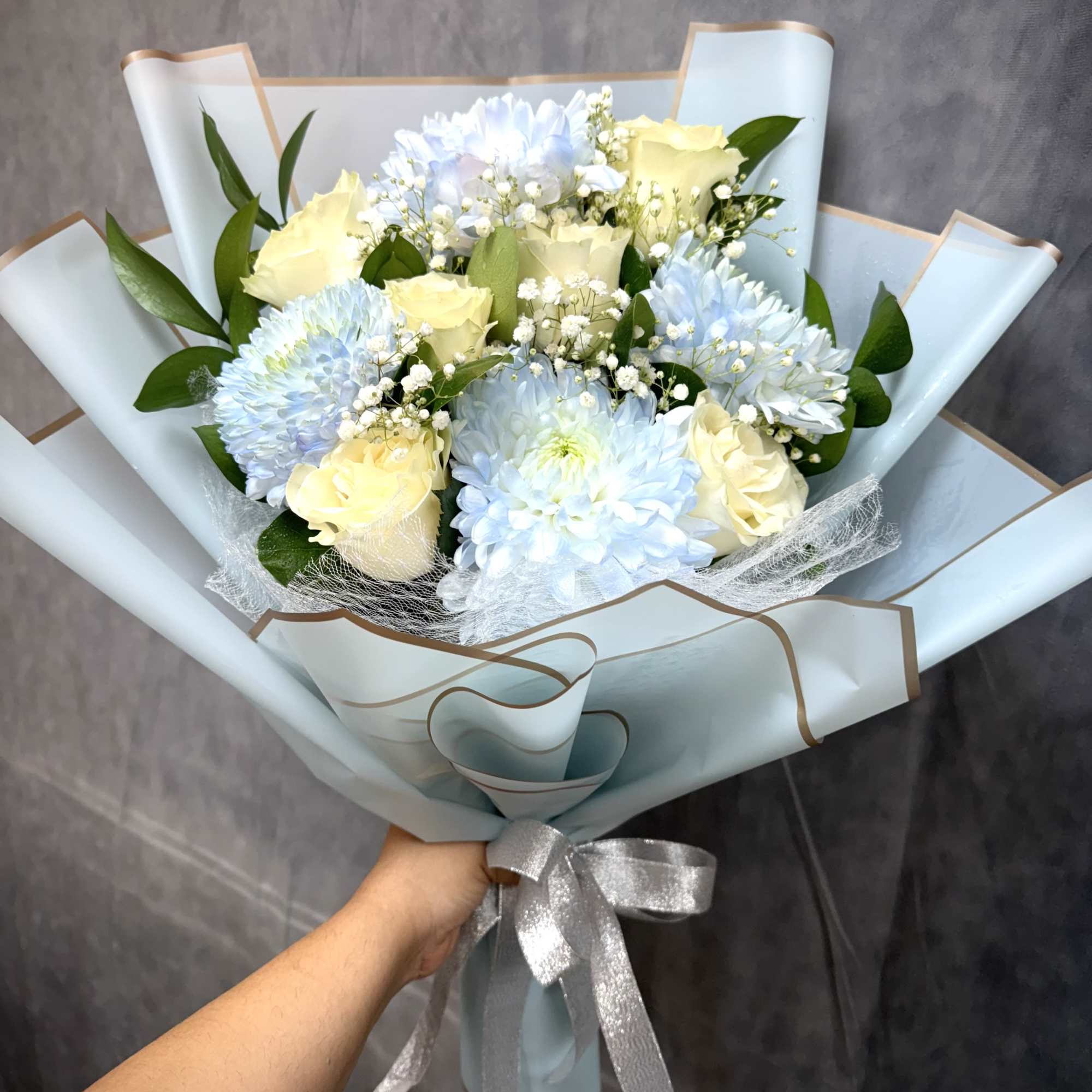 Bouquet of pale blue chrysanthemums and cream roses wrapped in light blue paper