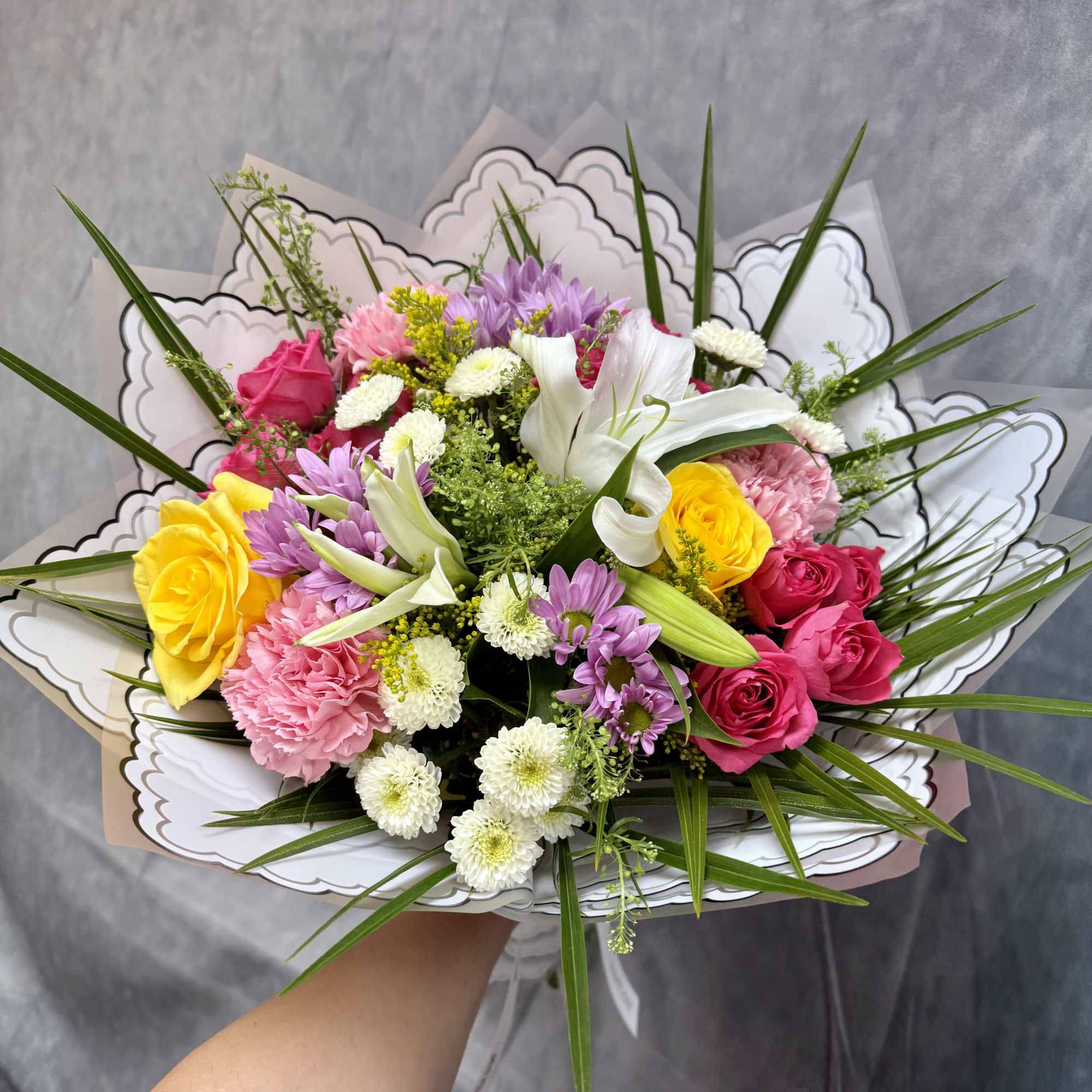 Mixed bouquet of roses, lilies, and daisies in decorative wrap