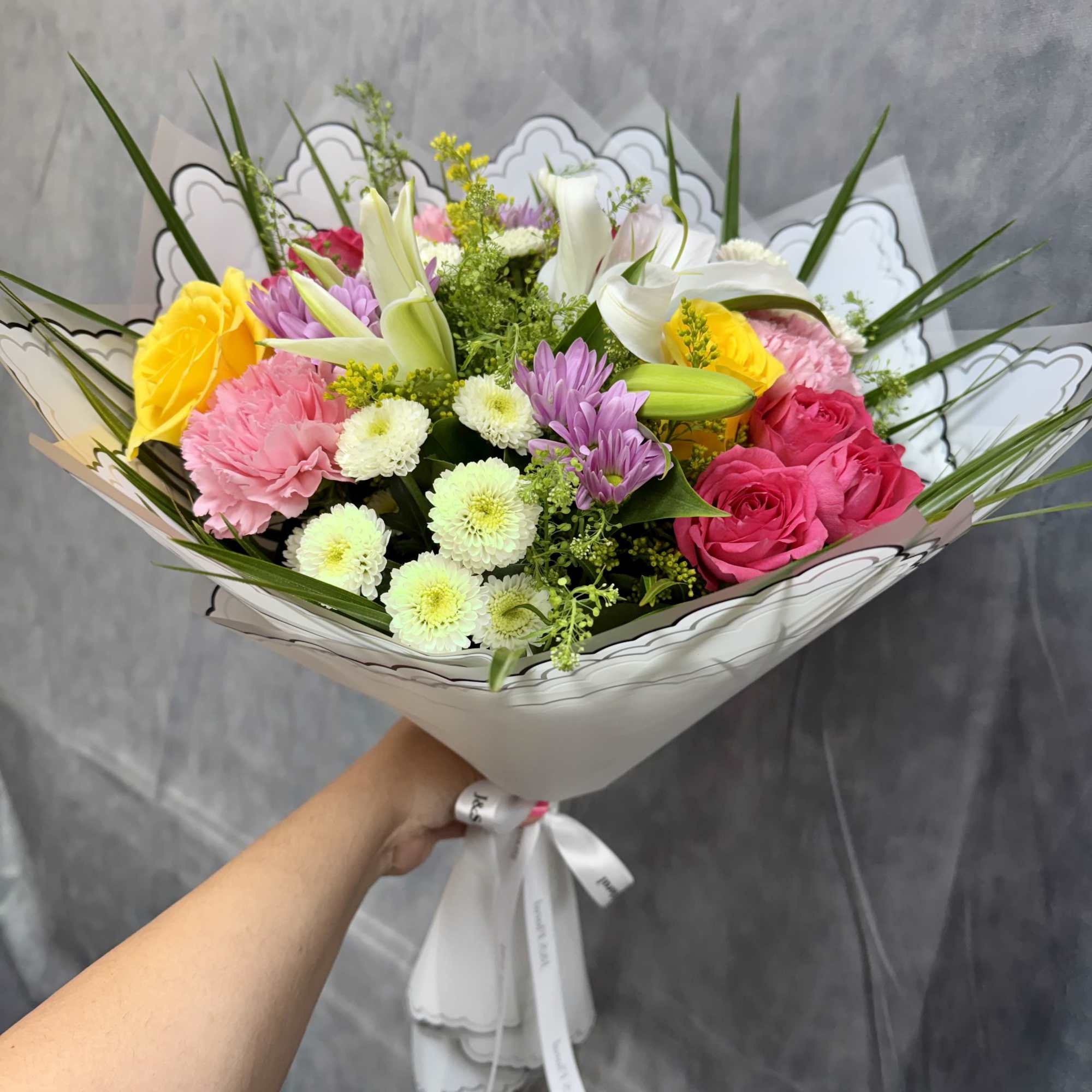 Bouquet of mixed pink, yellow, white, and purple flowers wrapped in white paper