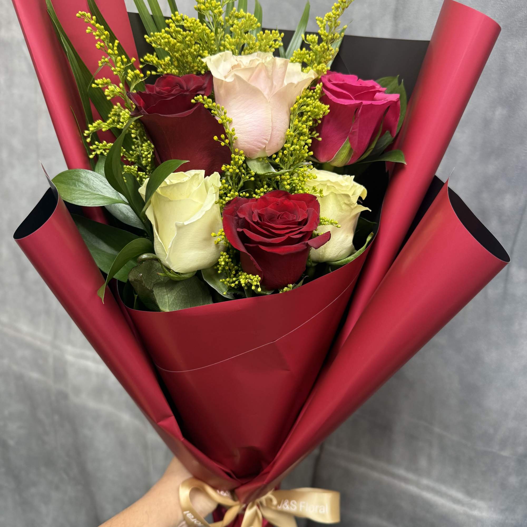 Bouquet of red, white, and pink roses wrapped in burgundy paper