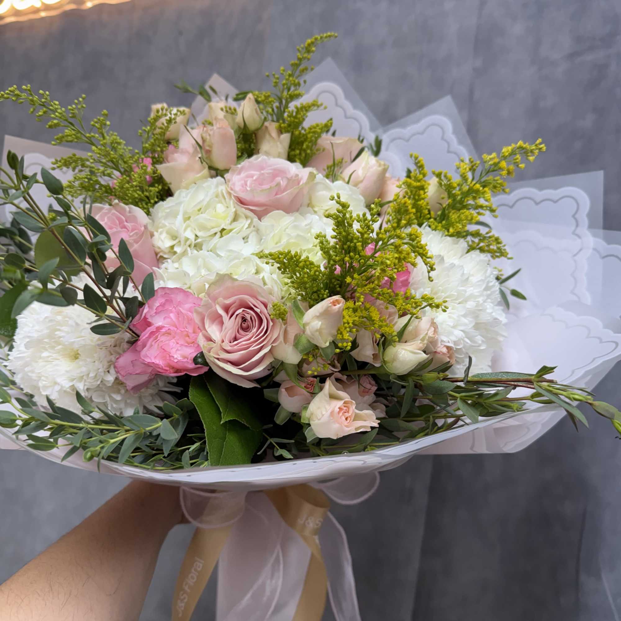 Handheld bouquet of pink and white roses with yellow filler flowers