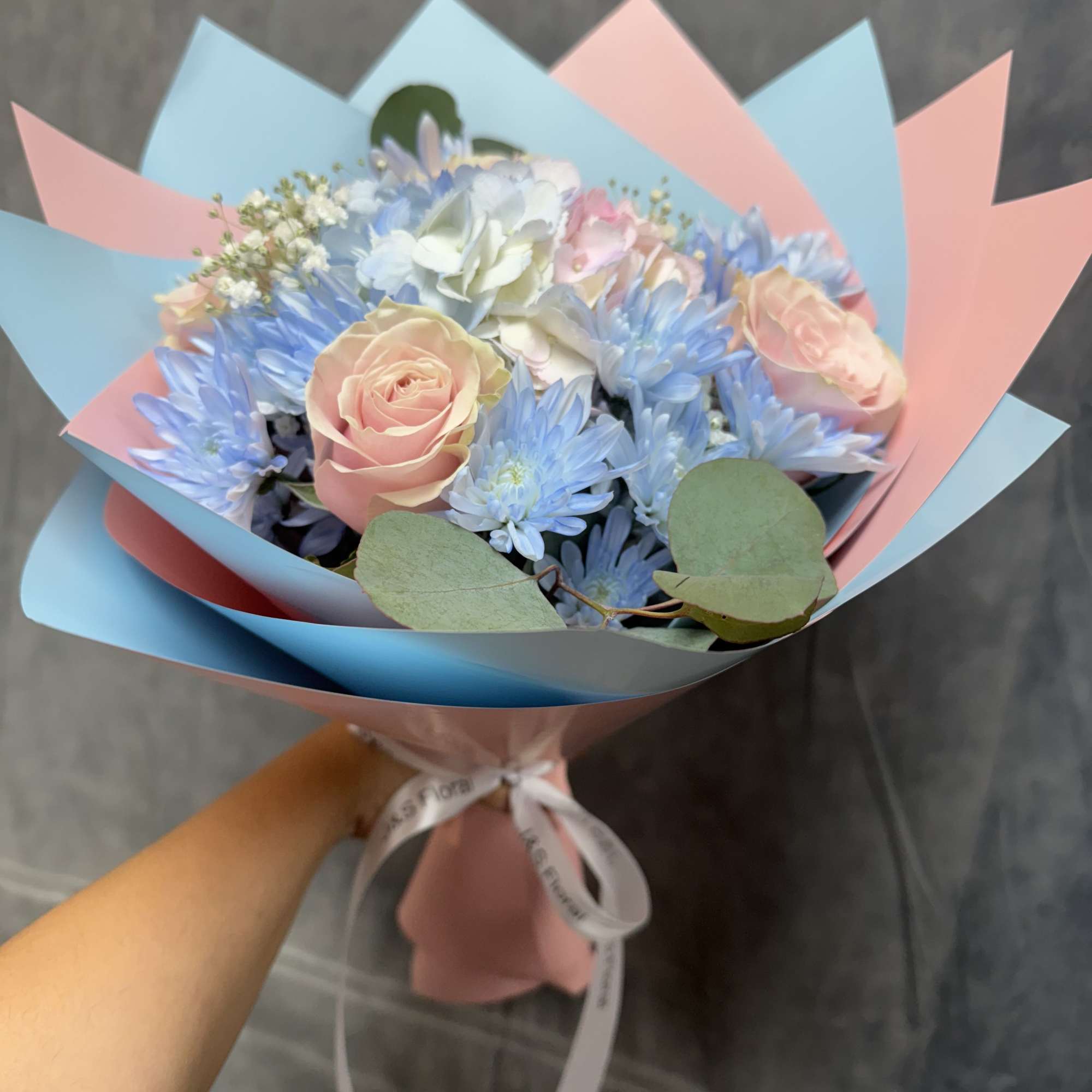 Pastel bouquet of pink roses and blue flowers wrapped in pink and blue paper