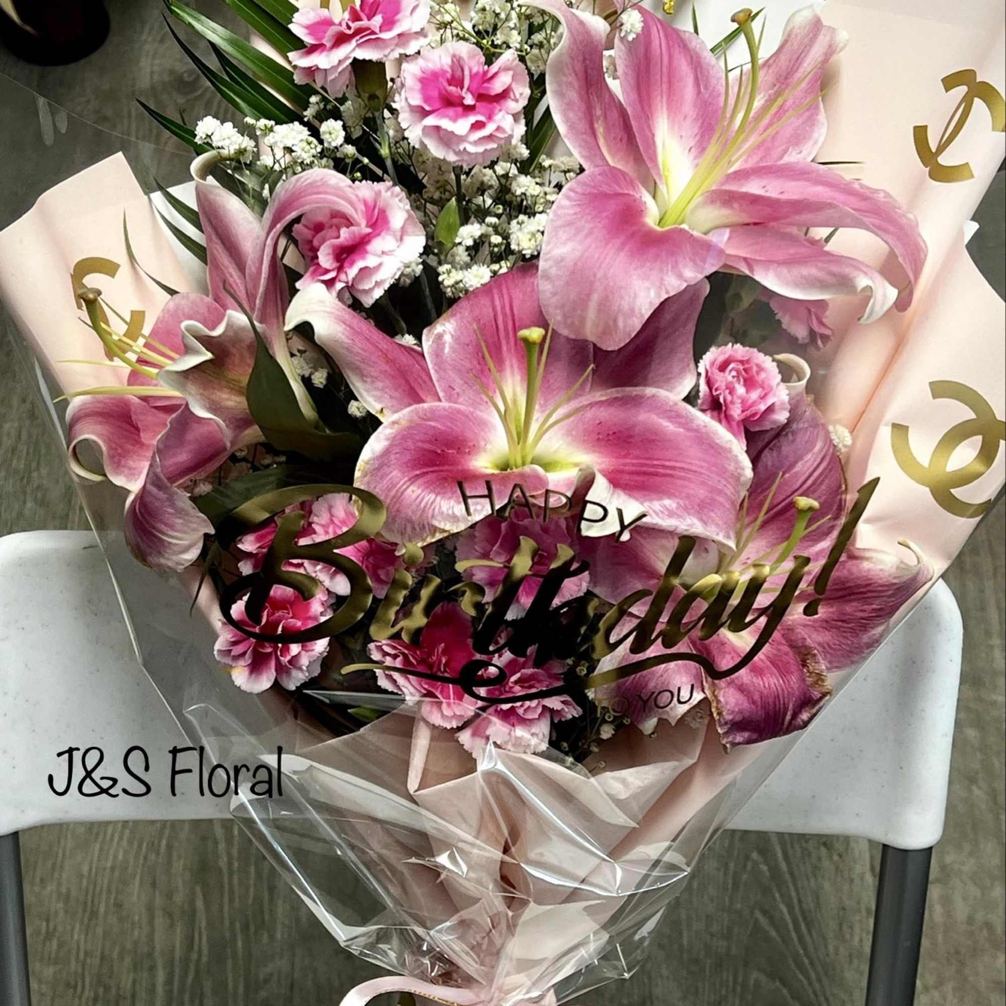 Pink lilies and carnations in a wrapped bouquet with a birthday topper