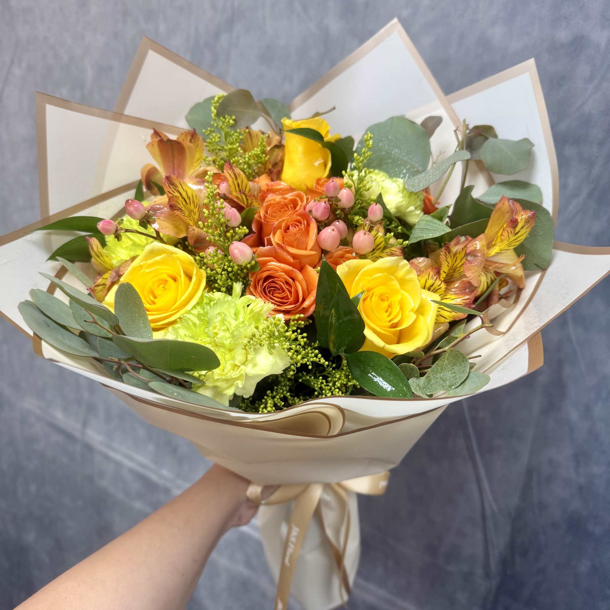 Bouquet of yellow and orange roses with pink accents in cream wrapping