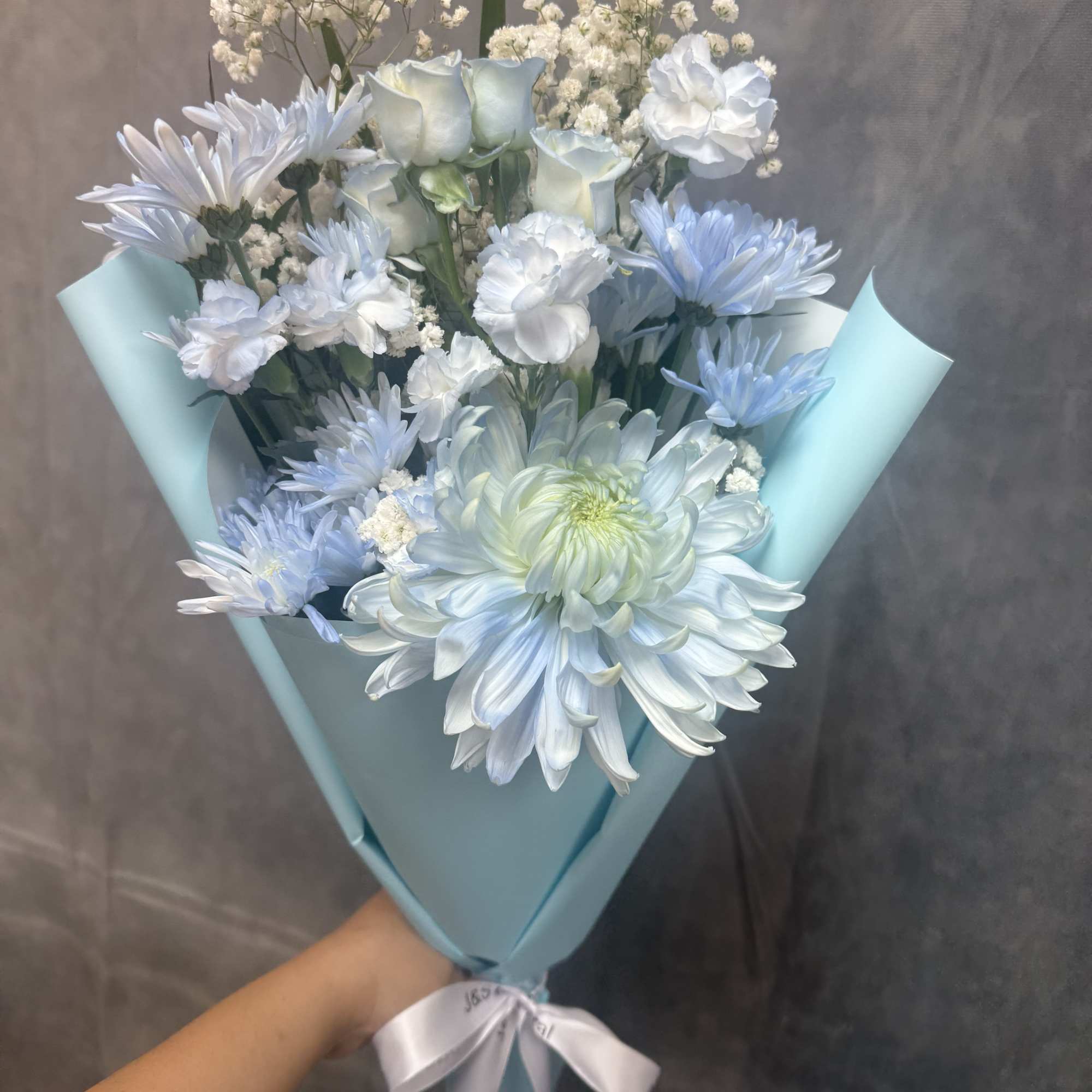 Pale blue, white and green bouquet of chrysanthemums, roses and carnations, hand-tied