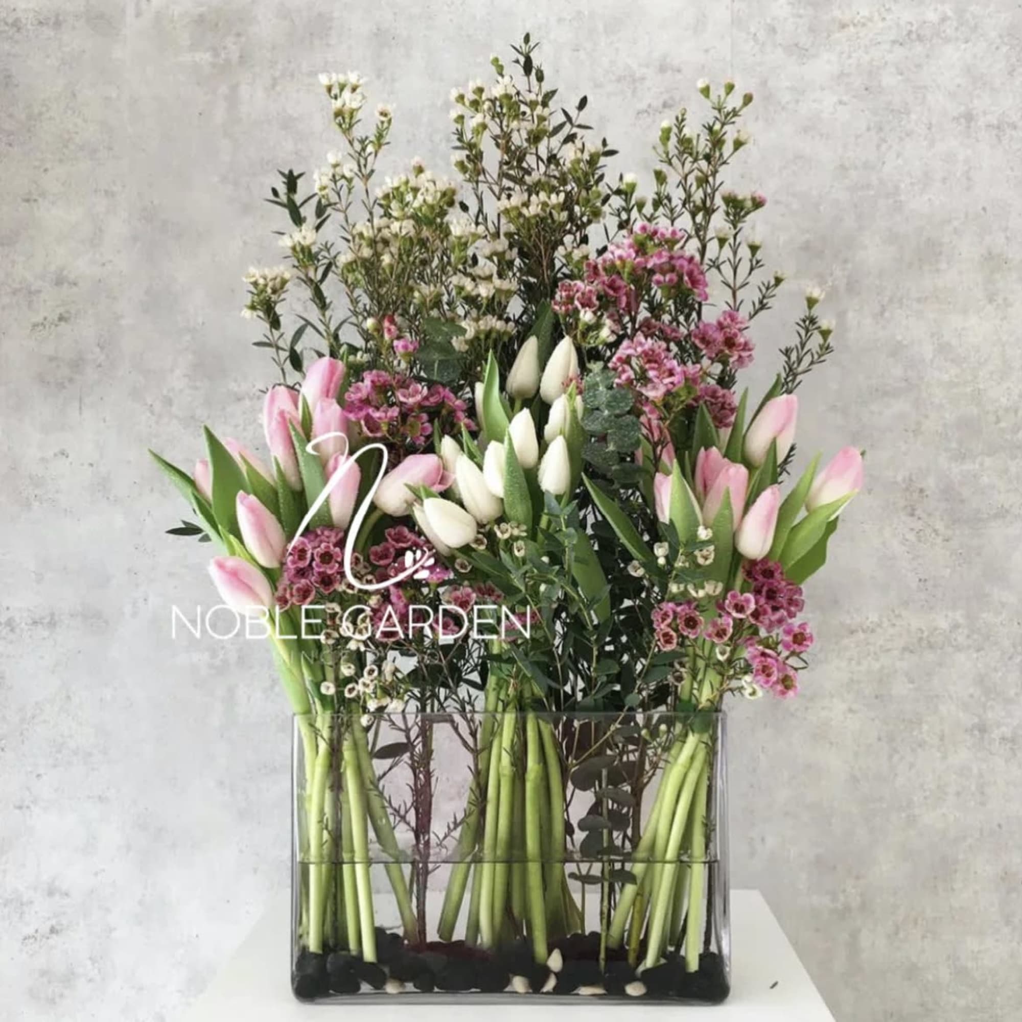 Tall floral arrangement with pink and white tulips in a clear rectangular vase