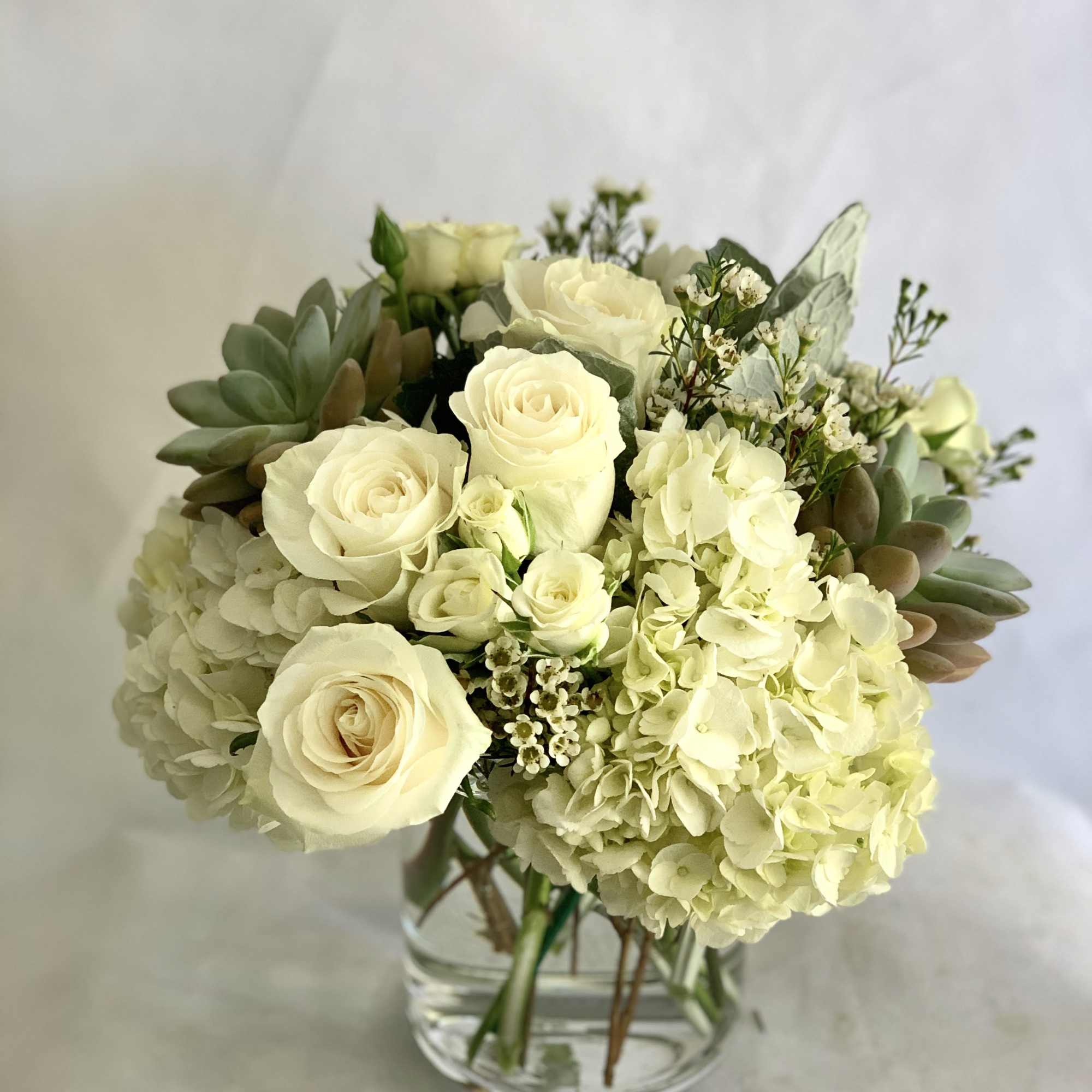 Cream roses and hydrangeas arranged in a clear glass vase