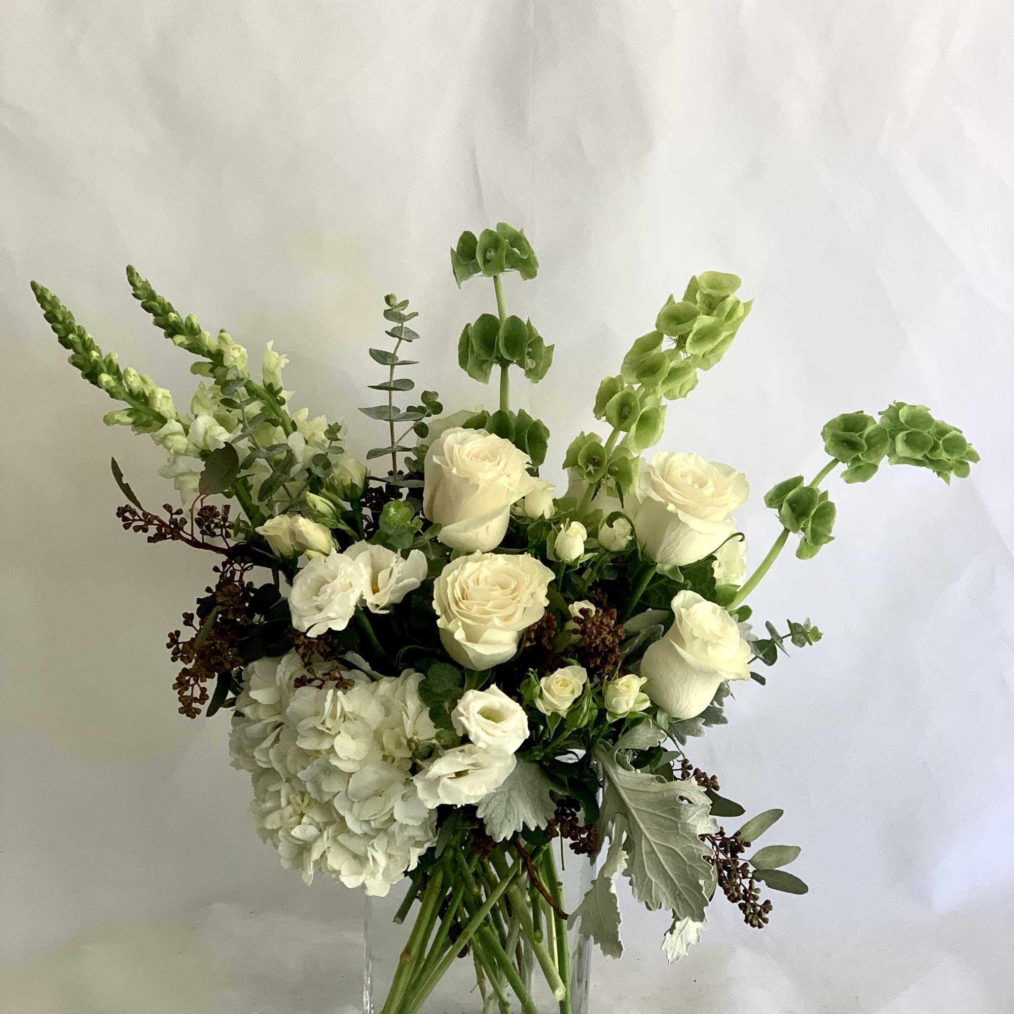 White floral arrangement in a clear square vase with tall green accents