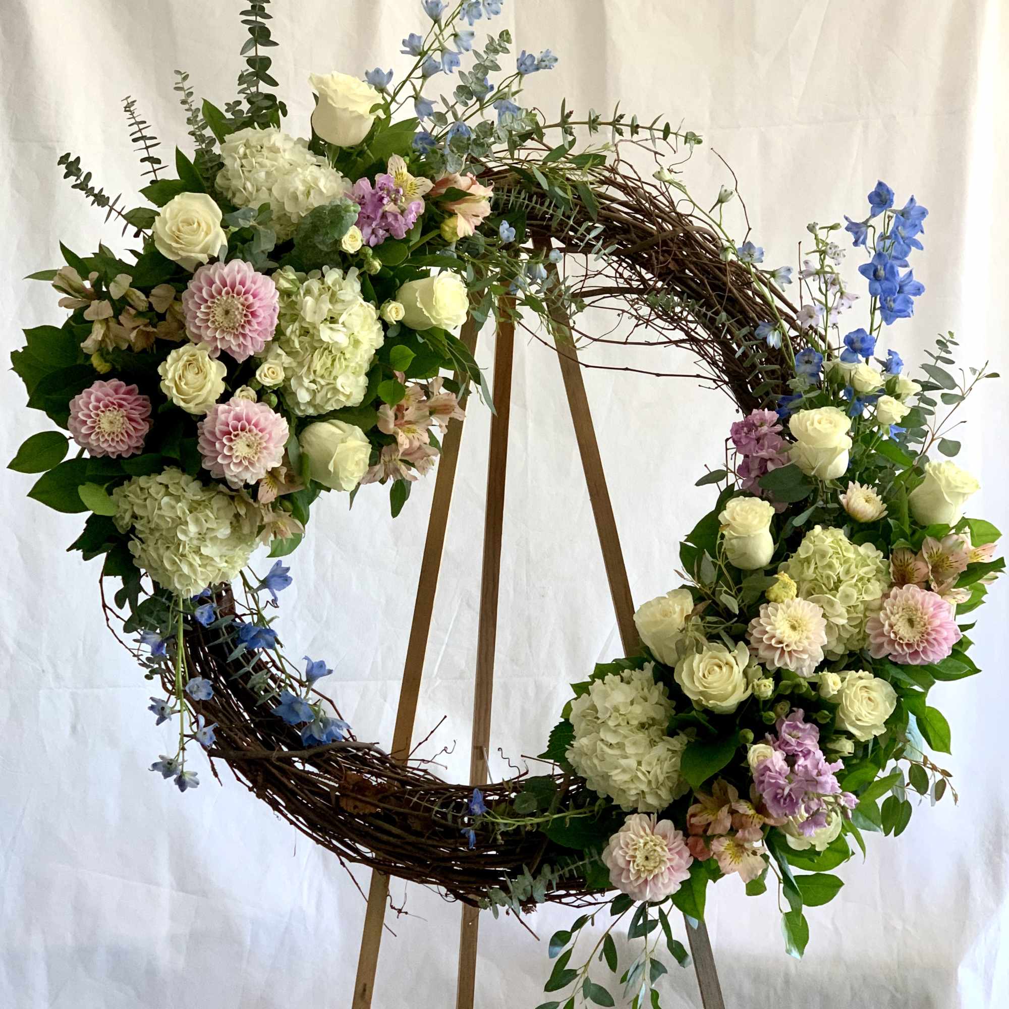 Large floral wreath with white, pink, and blue flowers on a wooden stand
