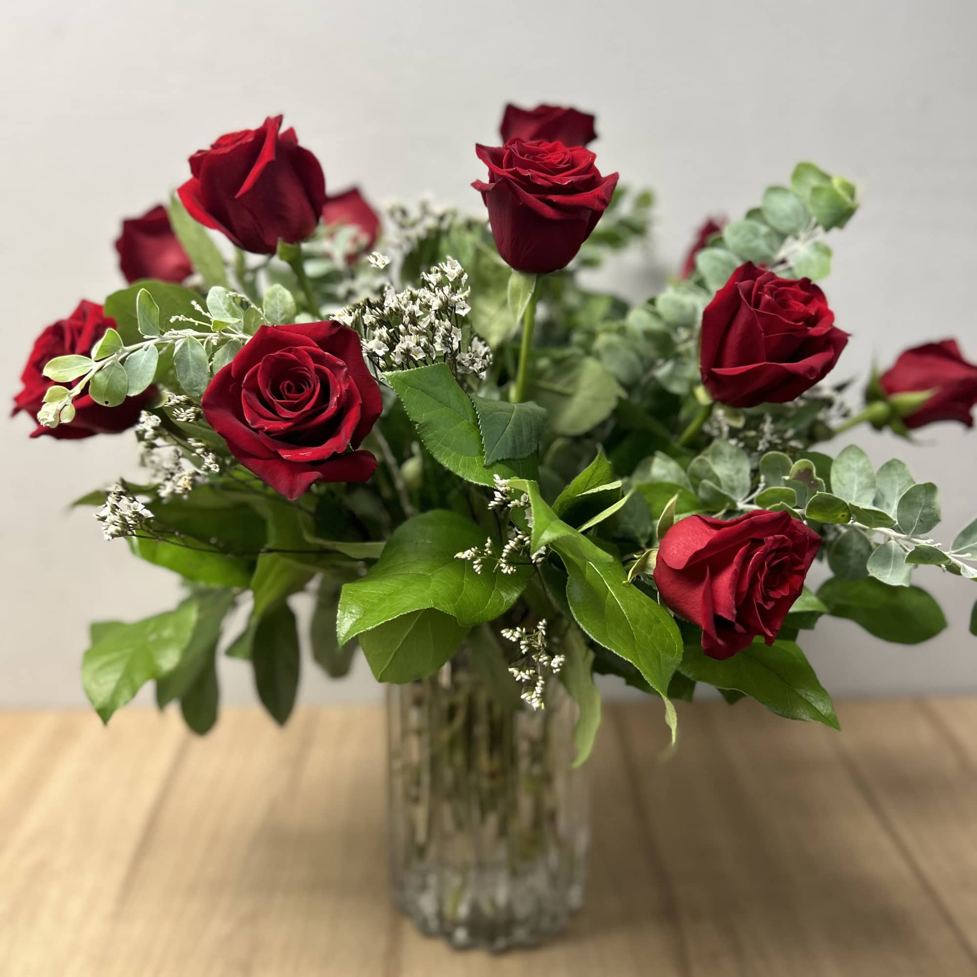 Red roses arranged in a clear glass vase with greenery