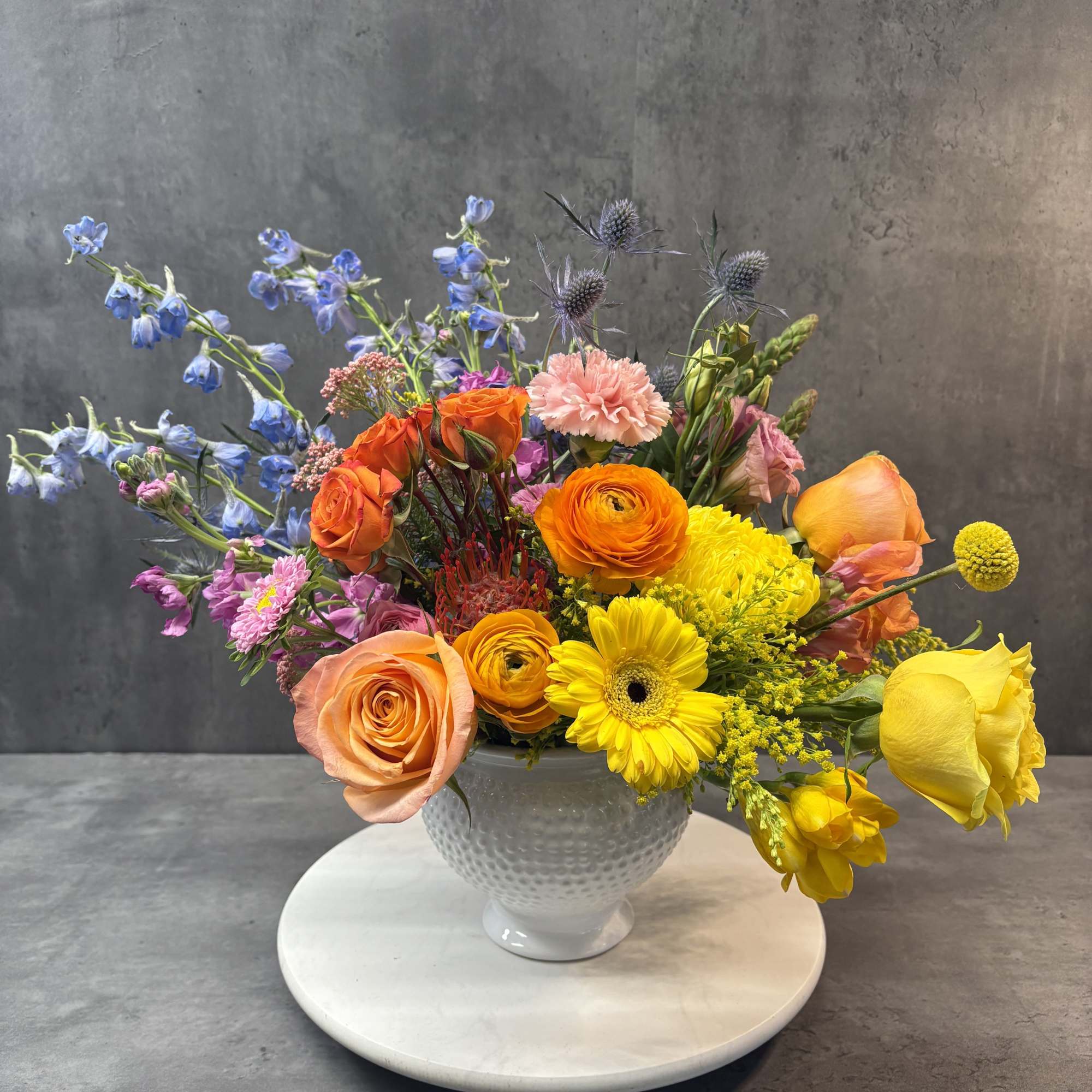 Mixed bouquet of orange, yellow, pink, and blue flowers in a white vase