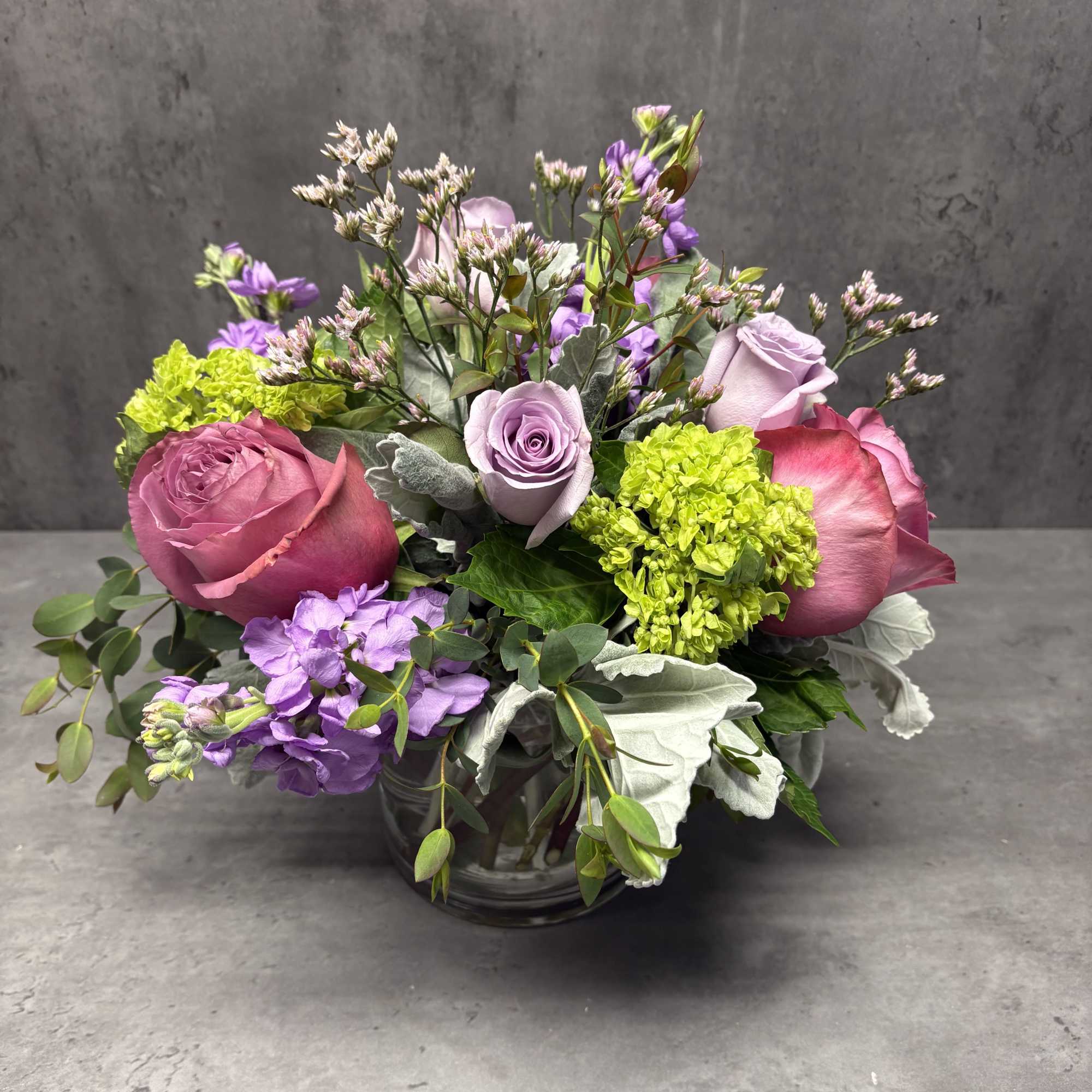 Pink and lavender roses arranged in a glass vase with purple blooms
