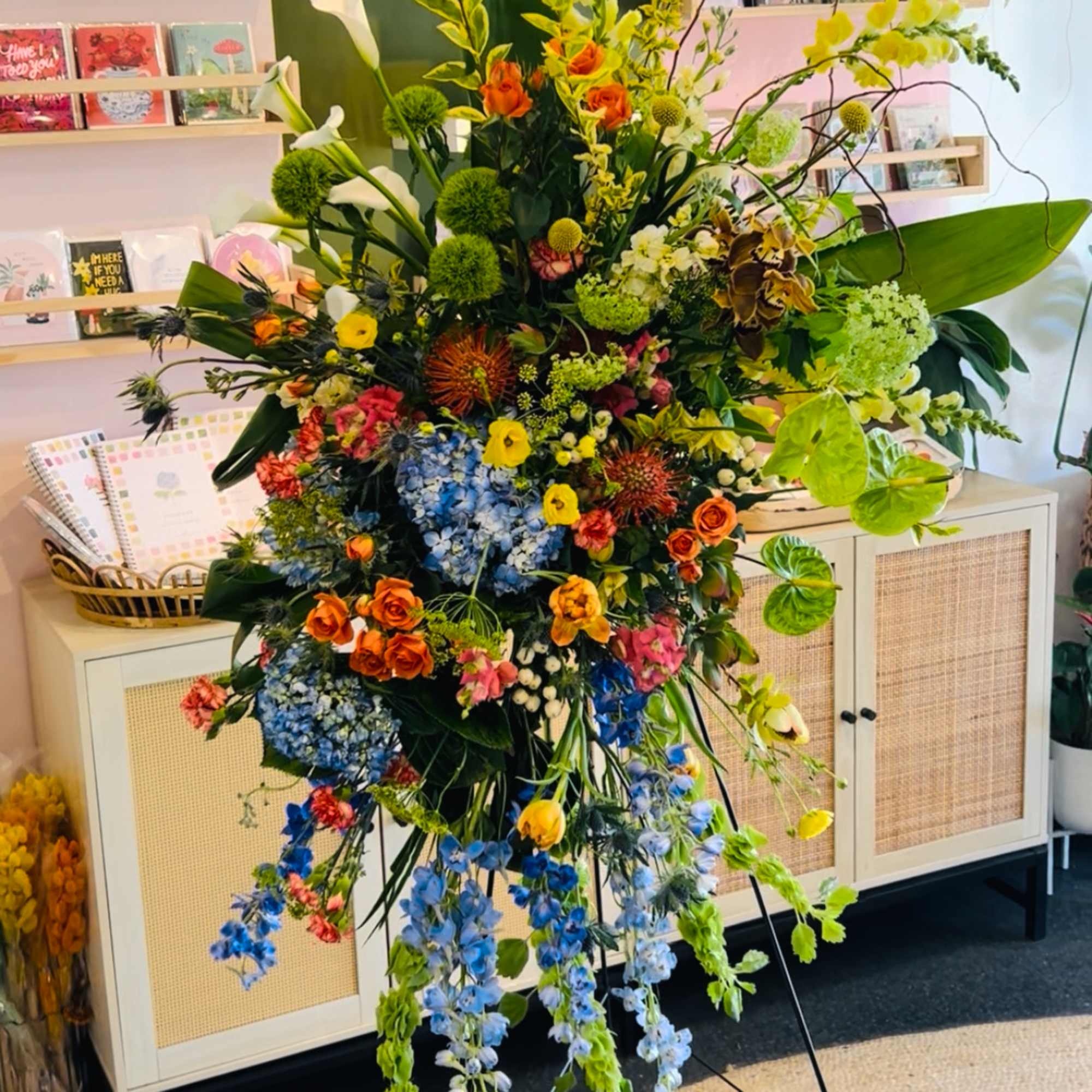 Tall standing floral arrangement with orange, blue, yellow, and white blooms