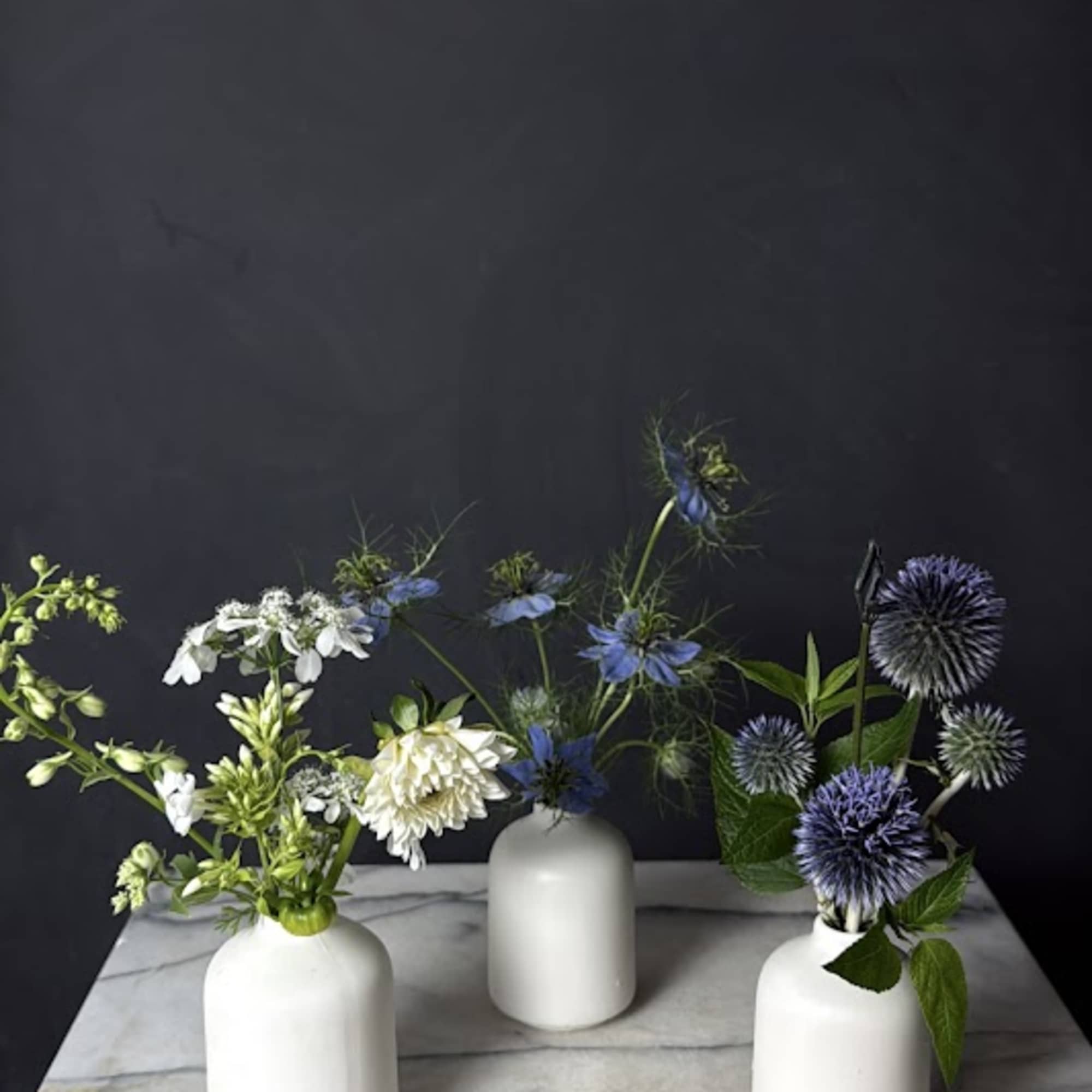 Three small floral arrangements in white vases on a marble surface