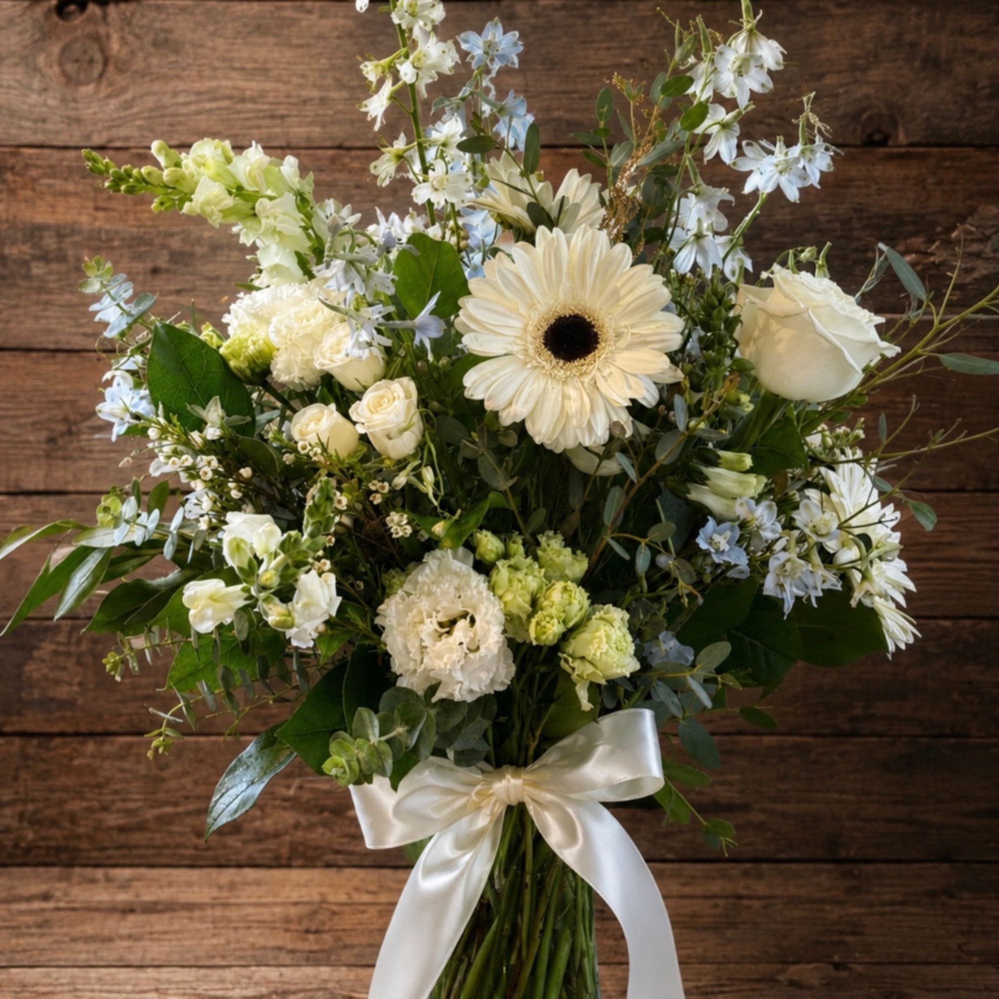 White and pale blue floral bouquet in a glass vase with a satin ribbon