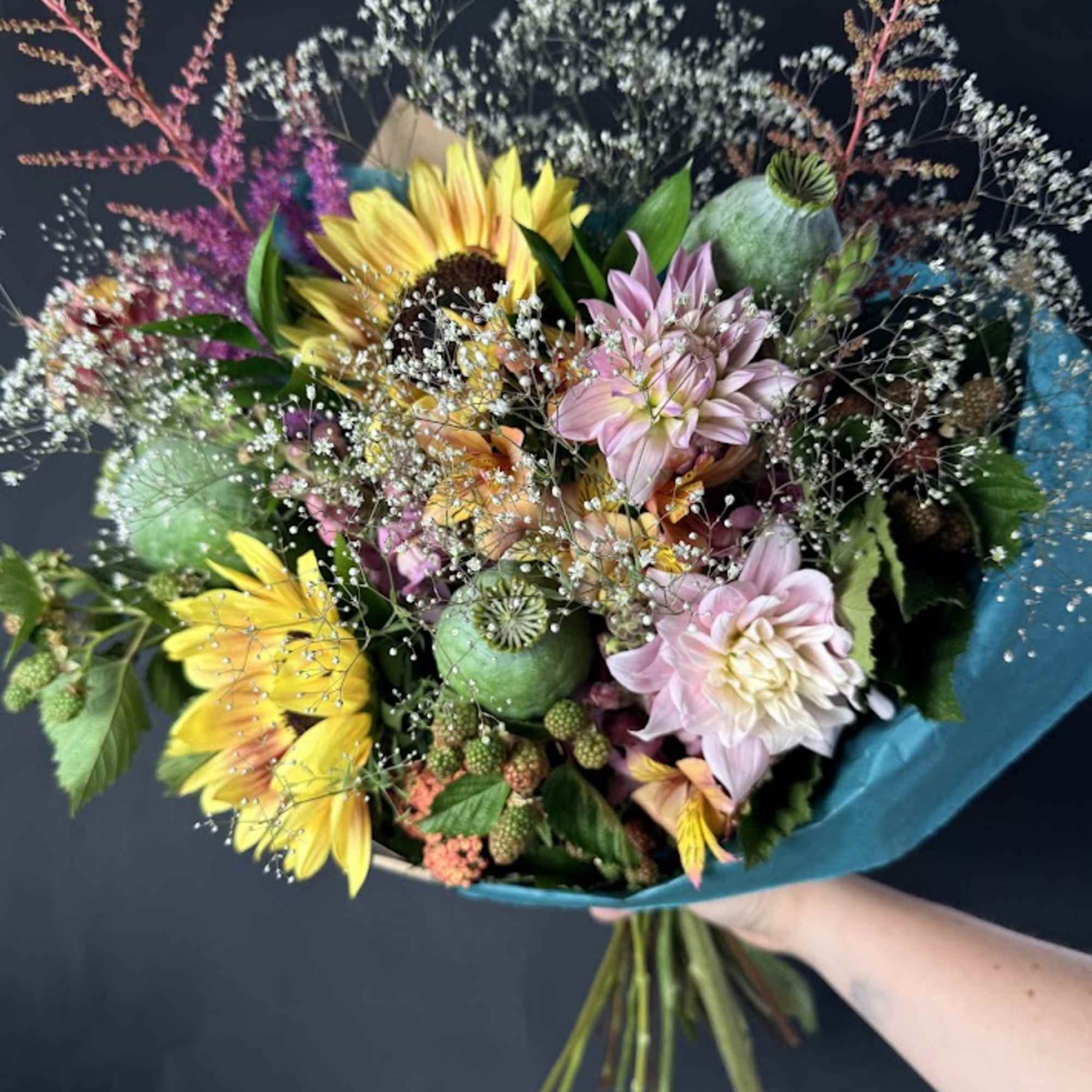 Handheld bouquet with yellow sunflowers and pink dahlias wrapped in teal paper