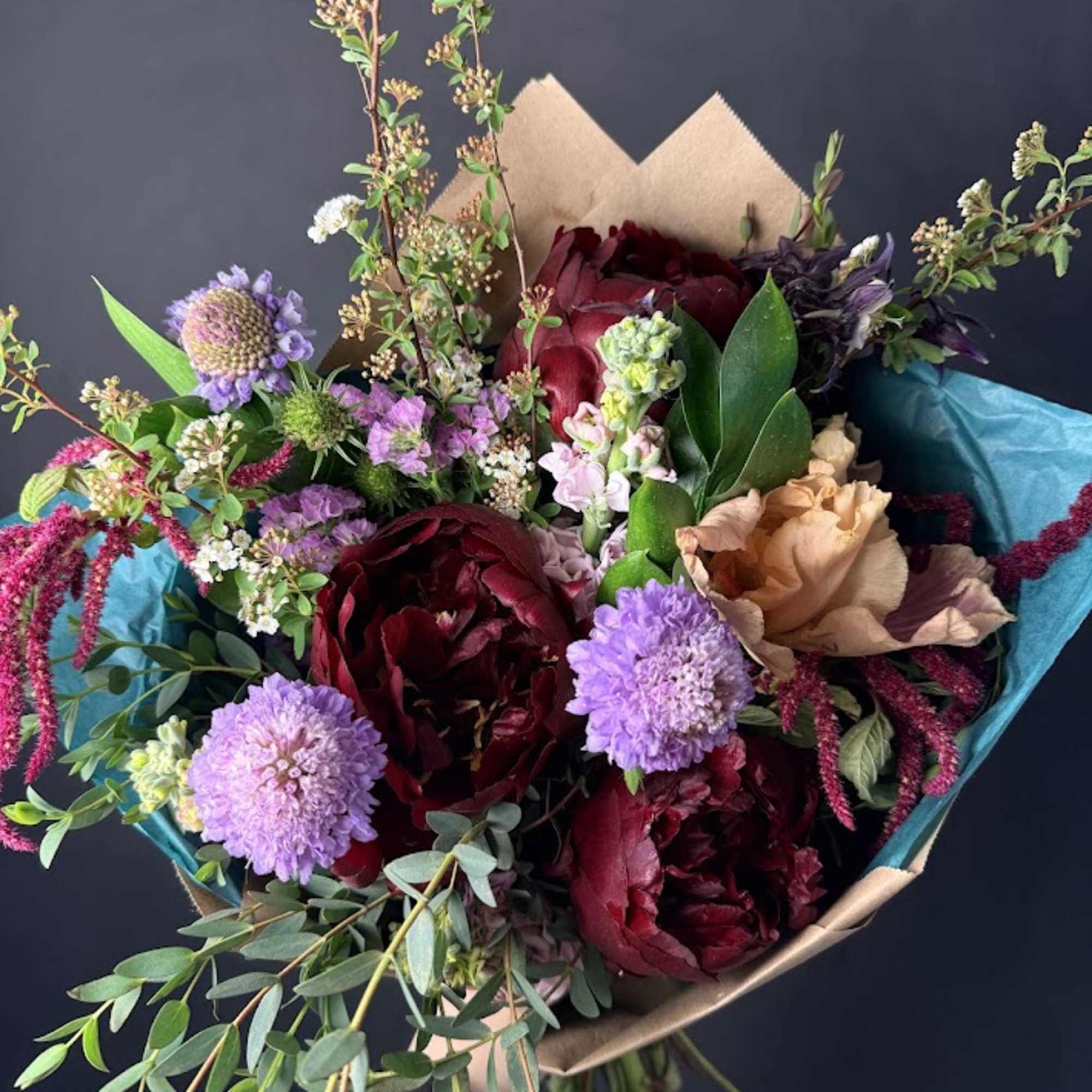 Handheld bouquet of burgundy and lavender flowers wrapped in paper
