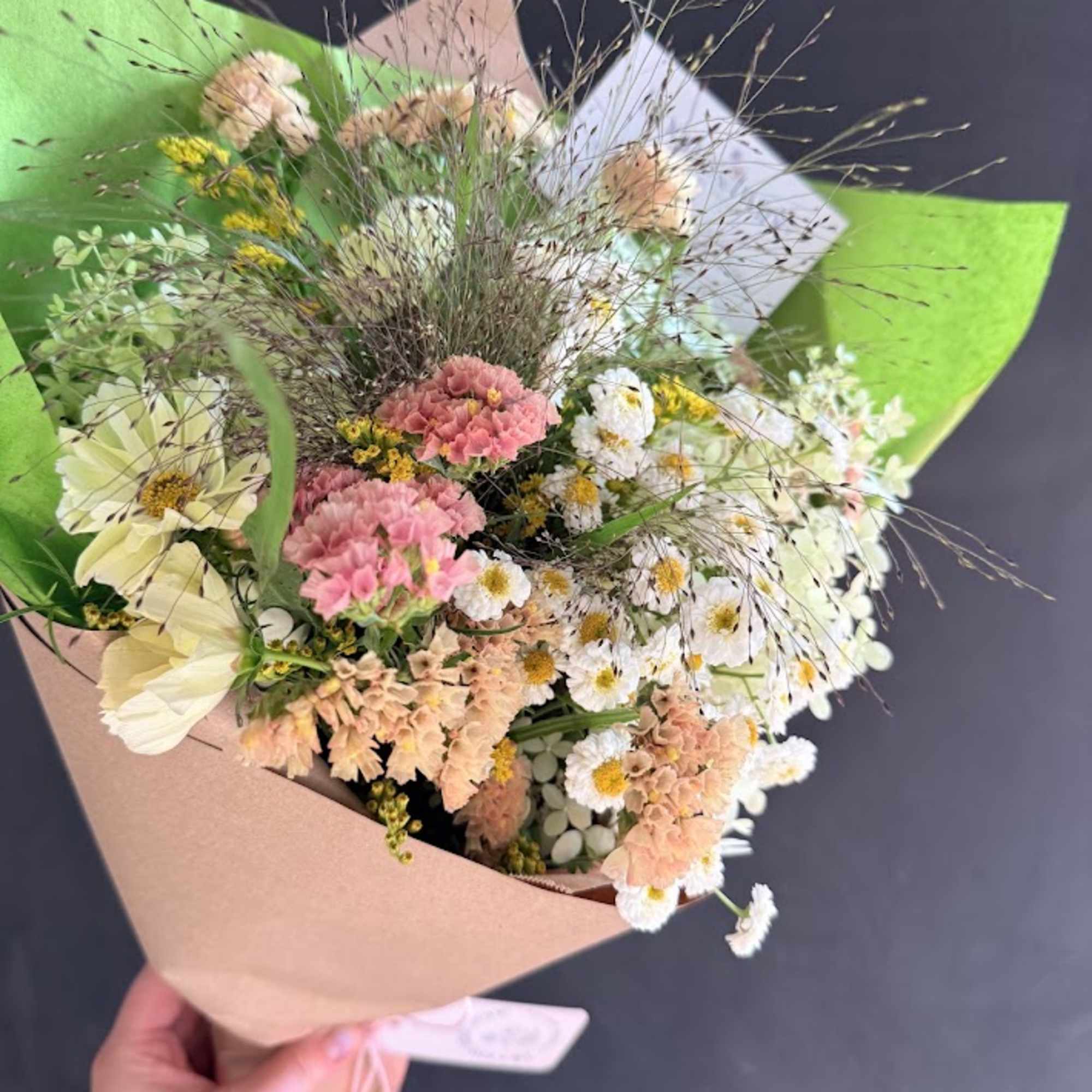 Handheld bouquet of pink, white, and peach flowers wrapped in paper