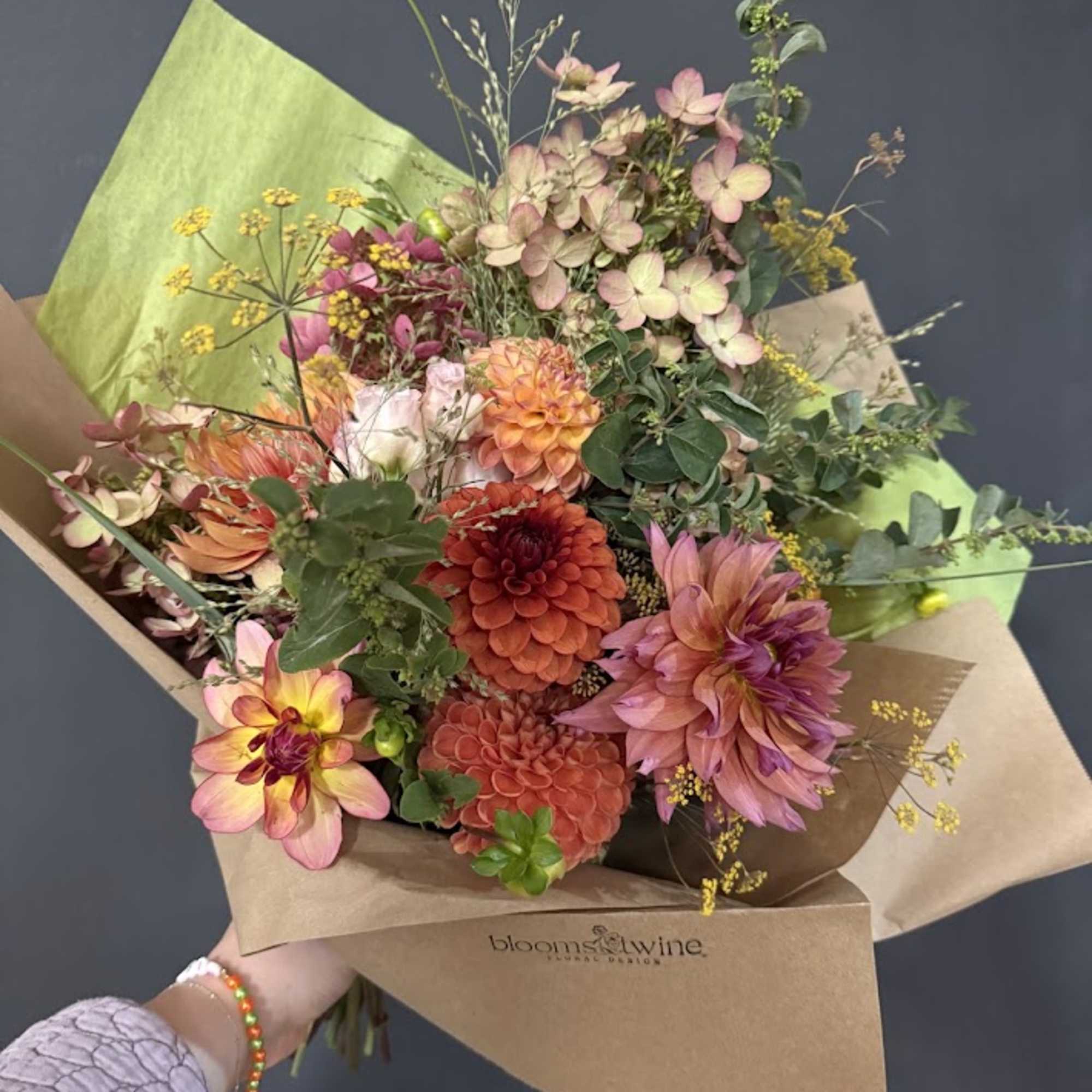 Hand-tied bouquet of pink and orange dahlias with mixed greenery